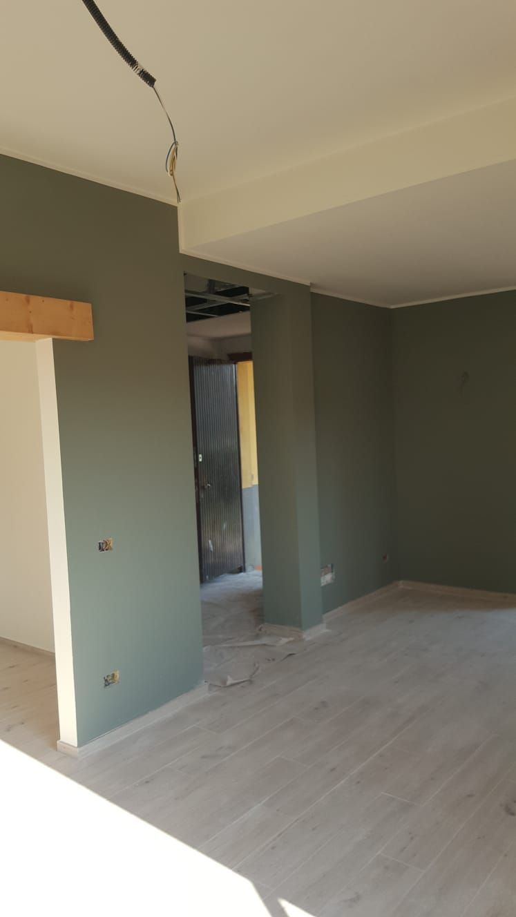 Stanza interna con pavimento in legno chiaro, pareti verde oliva, finiture bianche e porte aperte.