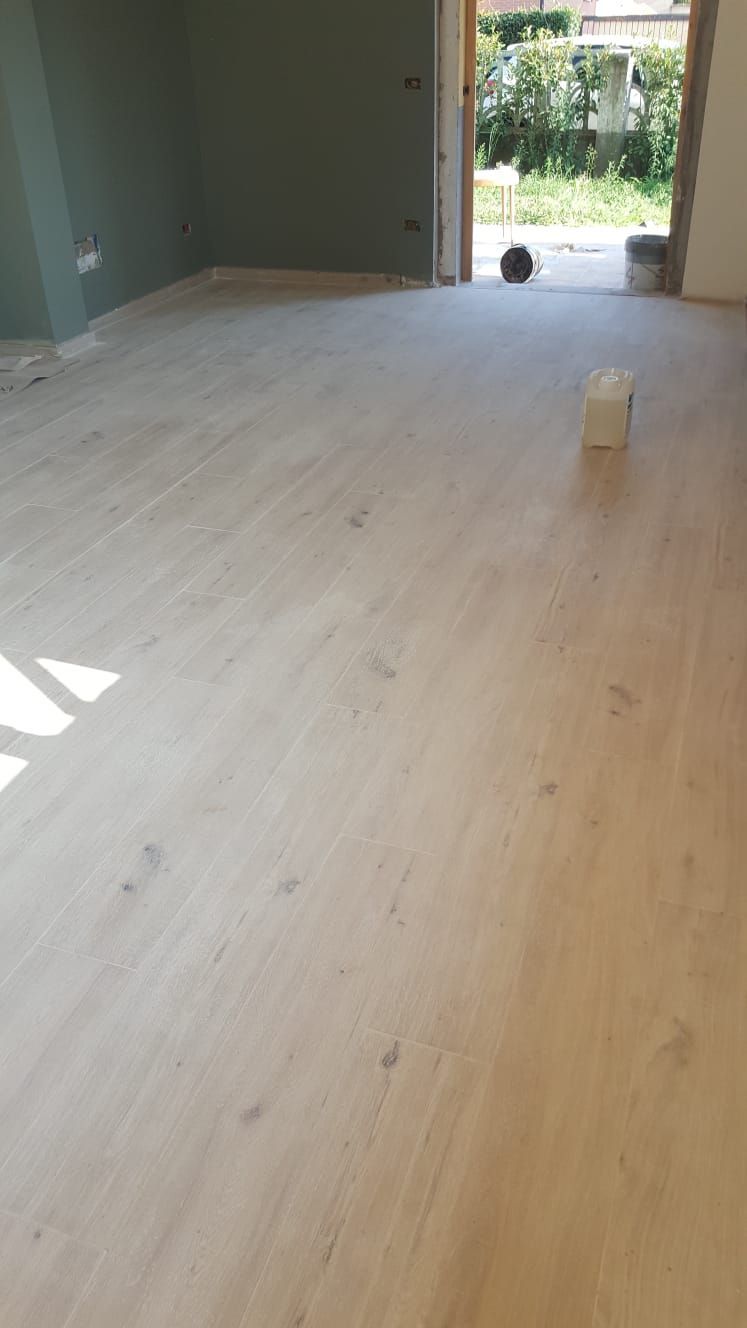 Pavimento in legno chiaro in una stanza con una parete verde e una porta aperta sull'esterno.