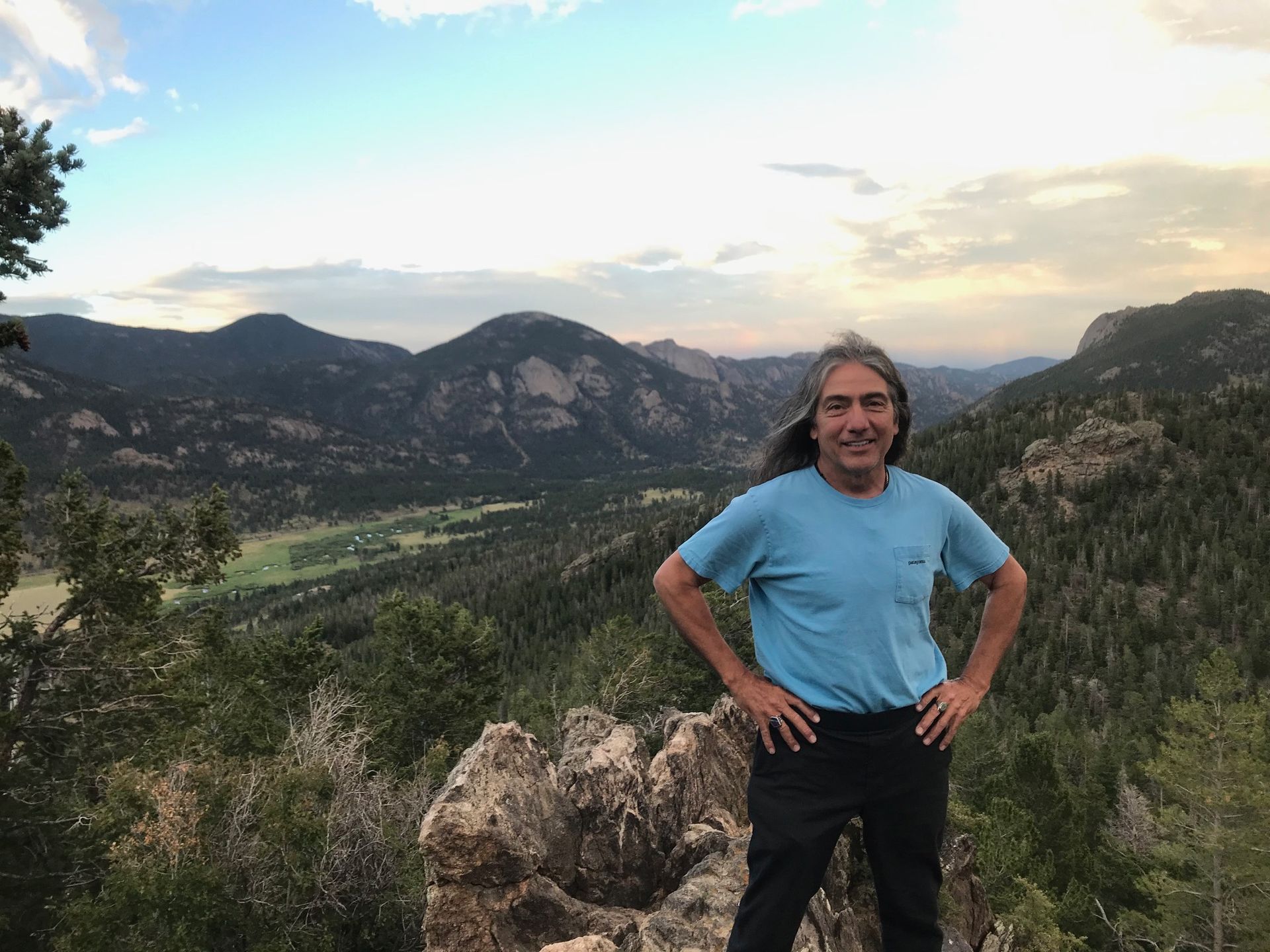 A man in a blue shirt is standing on top of a mountain.