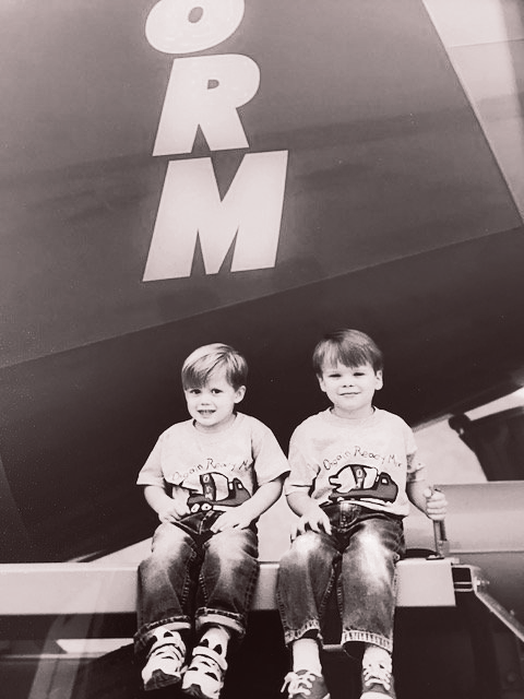 Two children sitting side by side on a ride, in front of a large ORM sign.