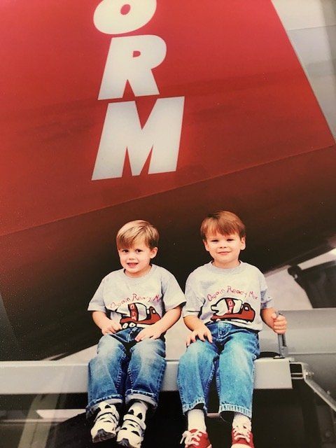 Two children sitting on a bench in front of a large red sign with white letters.