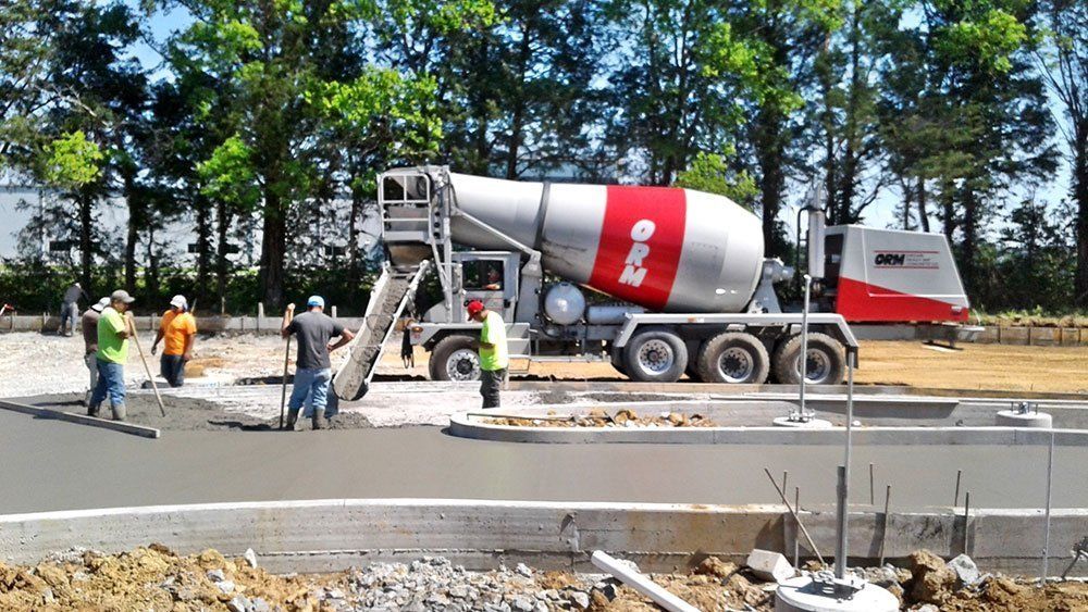Concrete mixer truck and workers at a road construction site beside a freshly paved curb