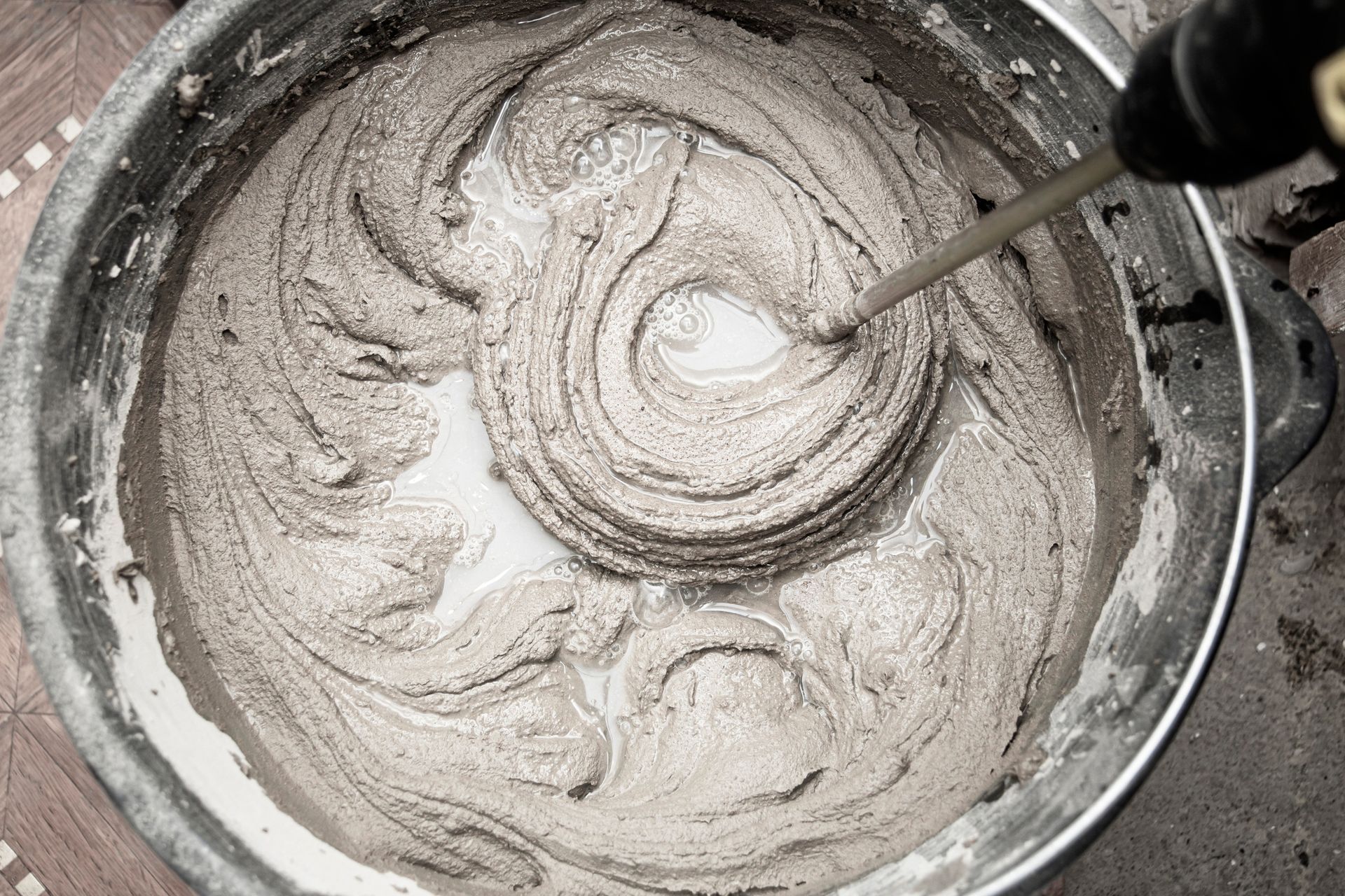 A hand mixer stirring gray batter in a metal bowl