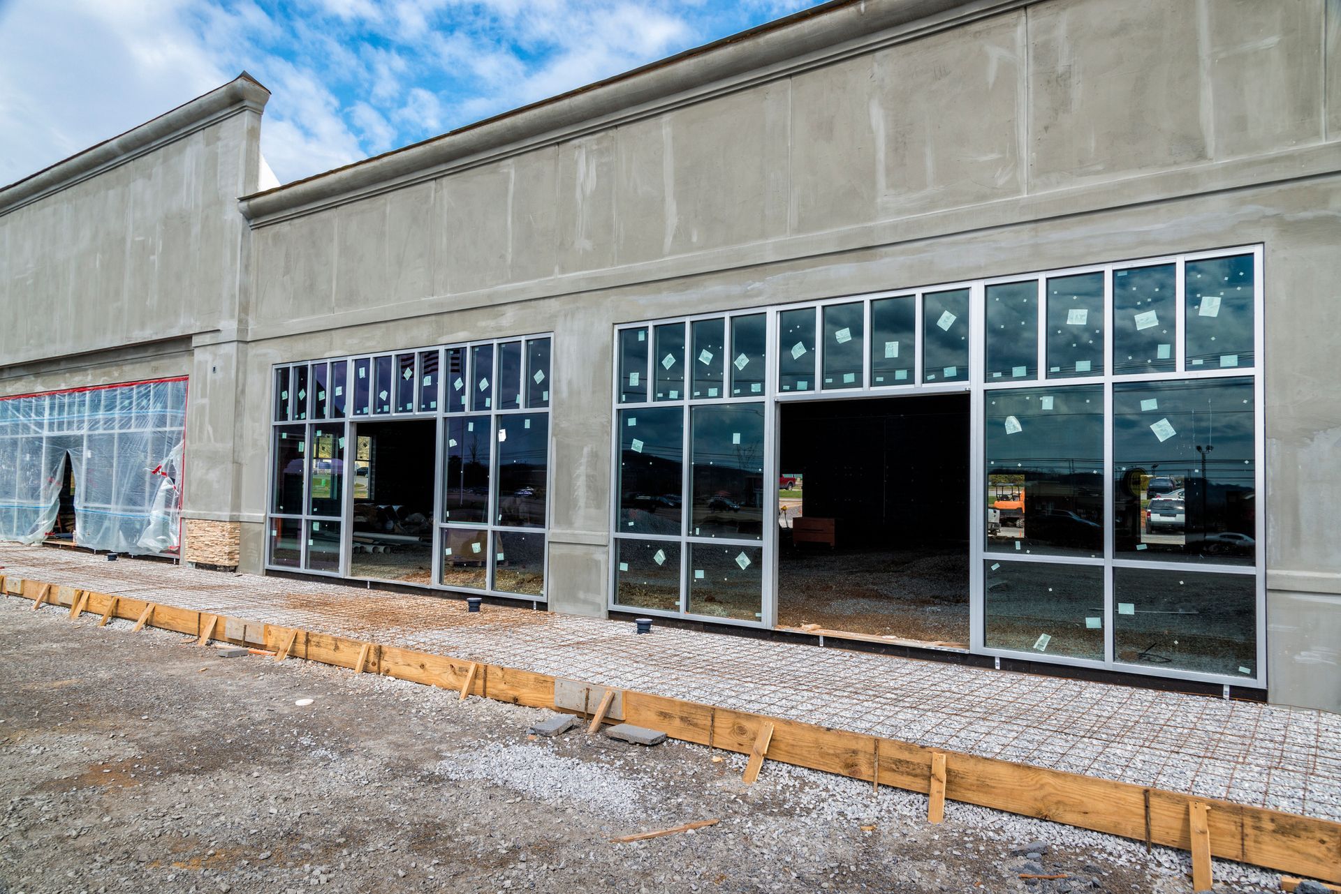 Storefront with large glass windows in a concrete building, viewed from the outside on a gravel lot.