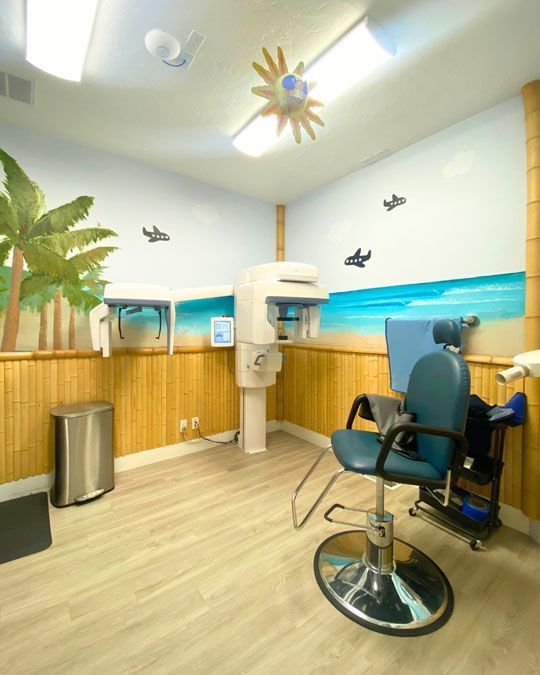 Dental exam room with blue chair, X-ray machine, and beach-themed wall decor