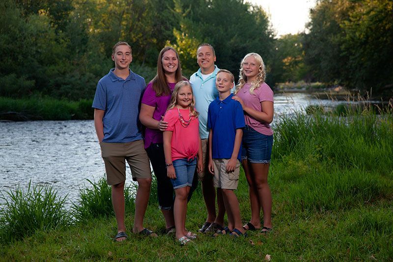 Five people posing by a river at sunset, with trees and water in the background.