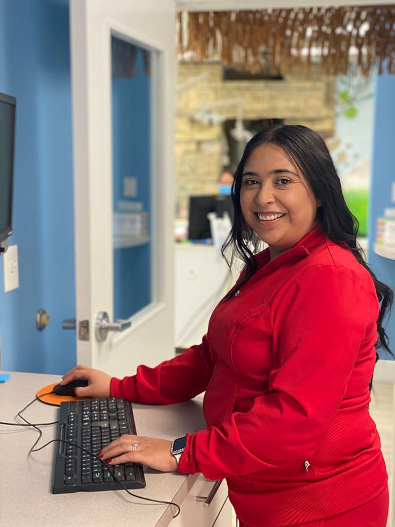 Woman in a red sweater smiling at a computer in an office hallway