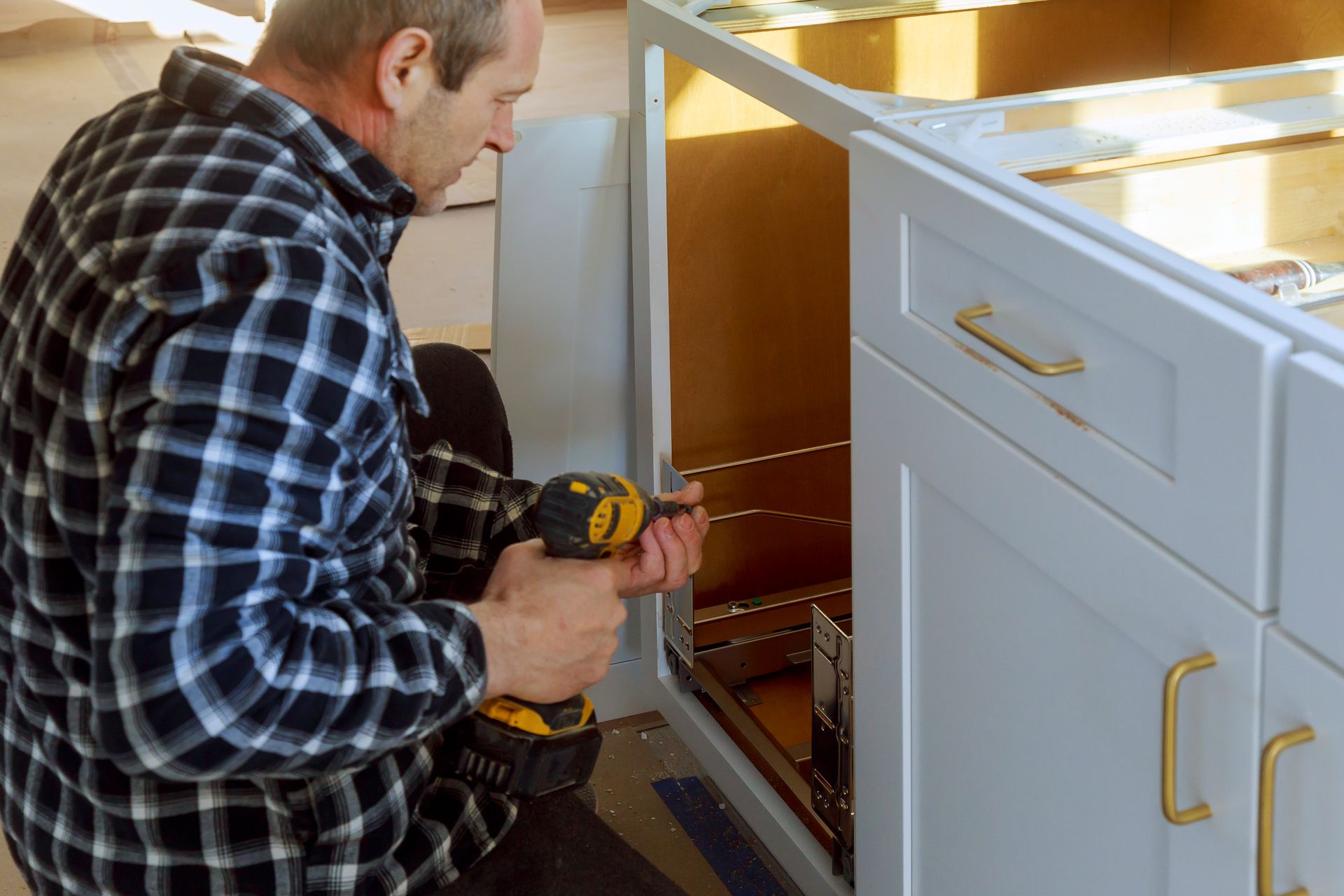A man is working on a kitchen cabinet with a drill.
