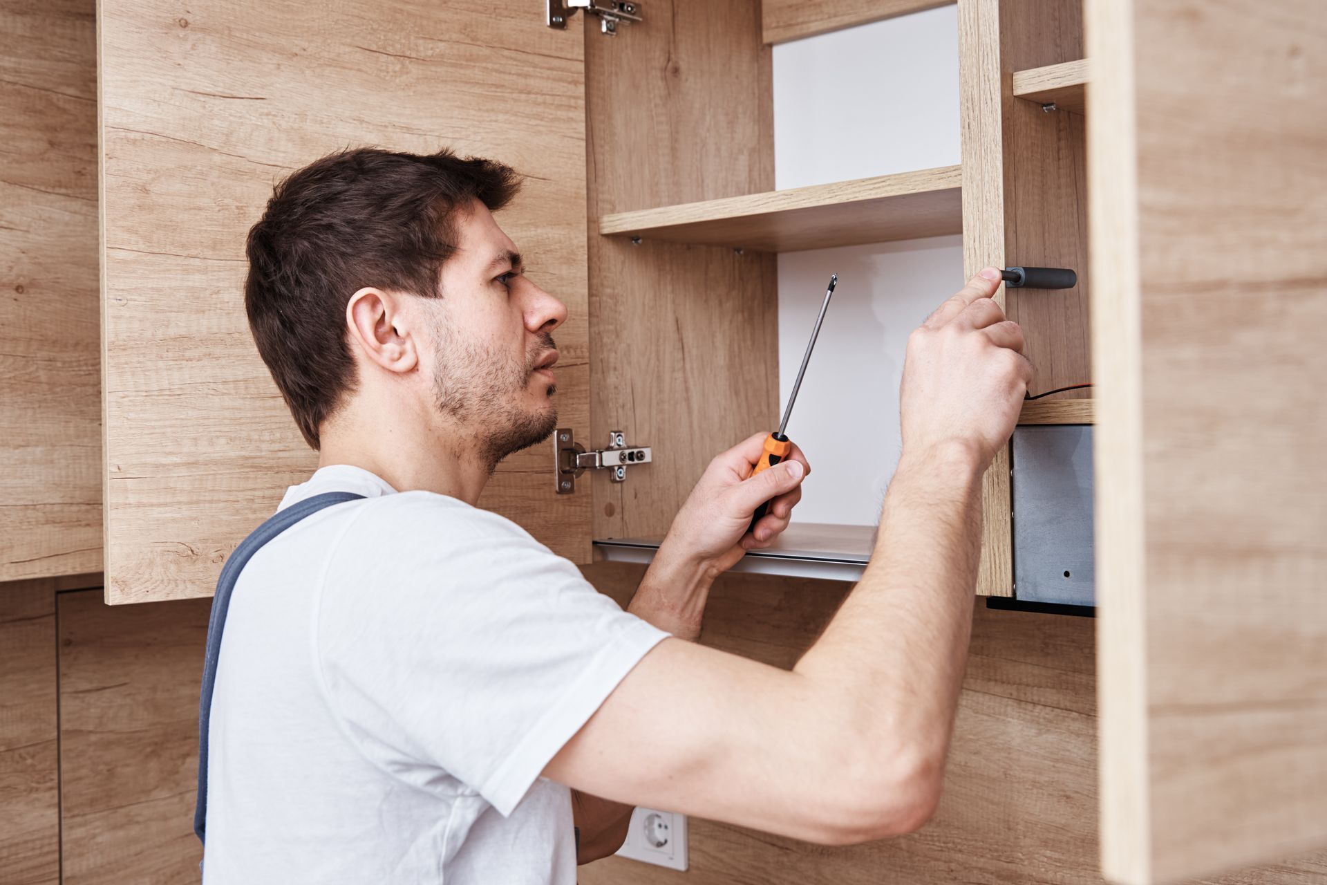 A man is fixing a cabinet with a screwdriver in a kitchen.