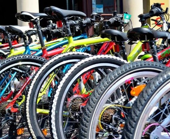File di biciclette colorate parcheggiate una accanto all'altra, con telai e ruote anteriori rossi, gialli e neri ben visibili.