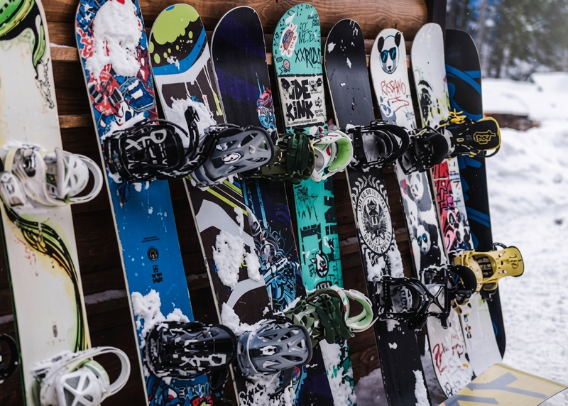Snowboard impilati verticalmente su una rastrelliera, con attacchi colorati e sfondi innevati.