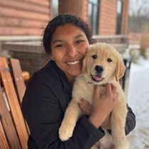 Smiling person holding a golden retriever puppy on a wooden bench outdoors.