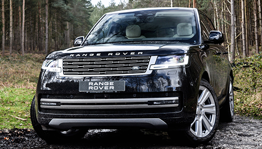 A black range rover is parked in the middle of a forest.