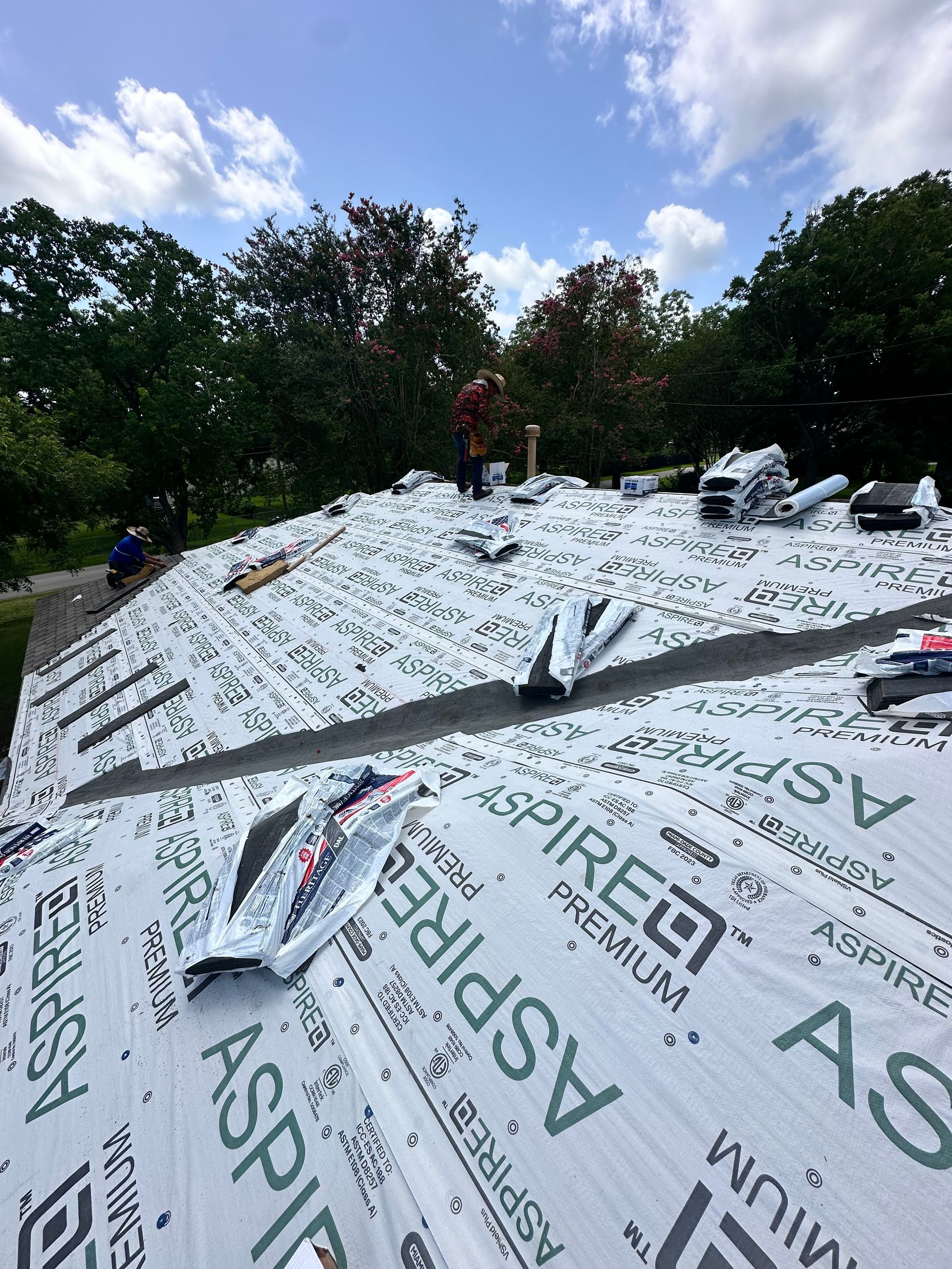 Roofing project: workers on a roof, installing underlayment with the forest in the background.