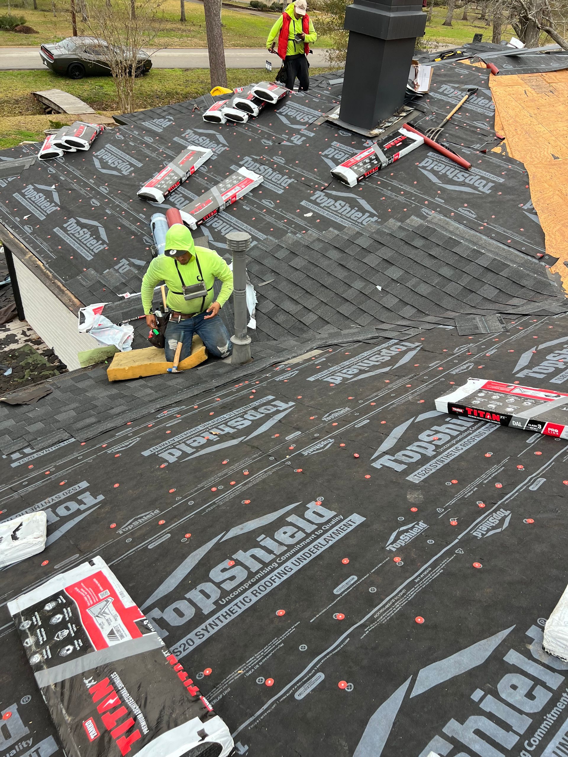 Roofers installing shingles on a roof, using tools and safety gear.