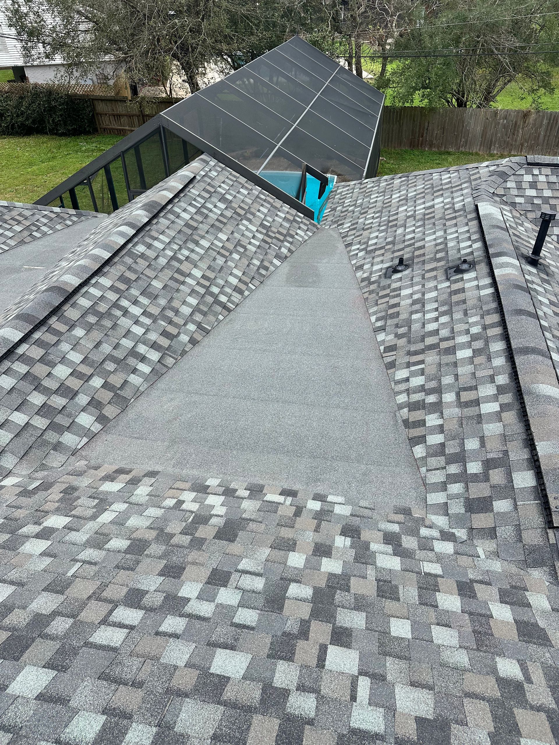 Roof with gray shingles, gravel-filled valley, and dark solar panels in the background.