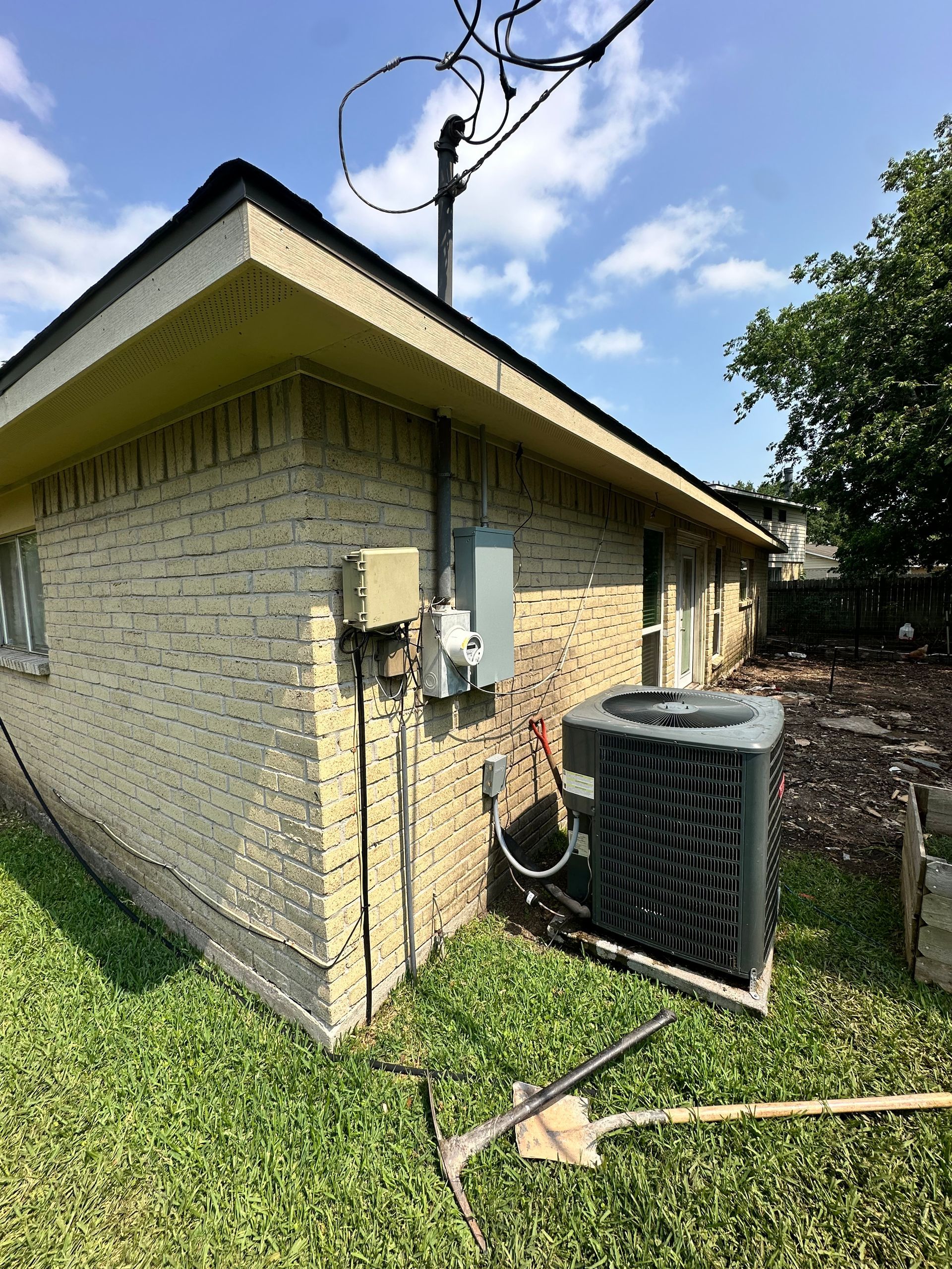 Exterior of a brick building with an AC unit, electrical boxes, and a utility pole in a grassy yard.