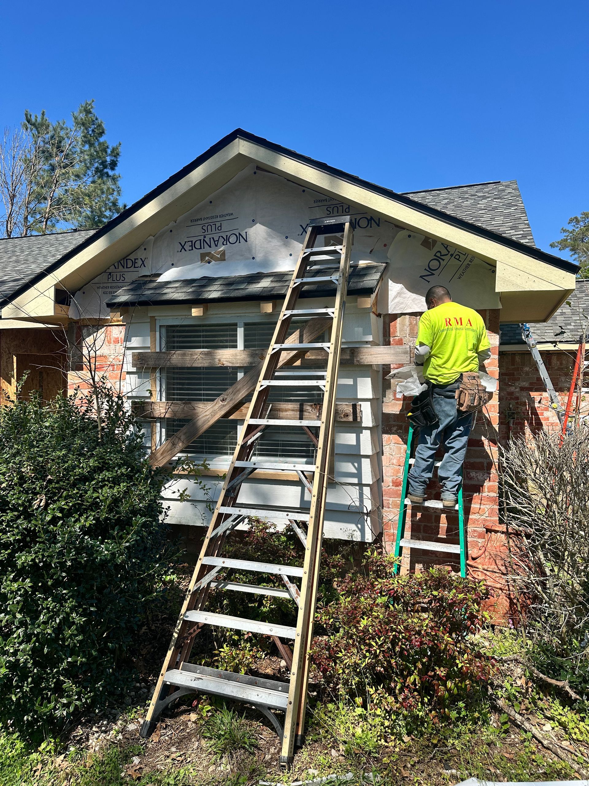 Construction worker on ladder repairing house siding.