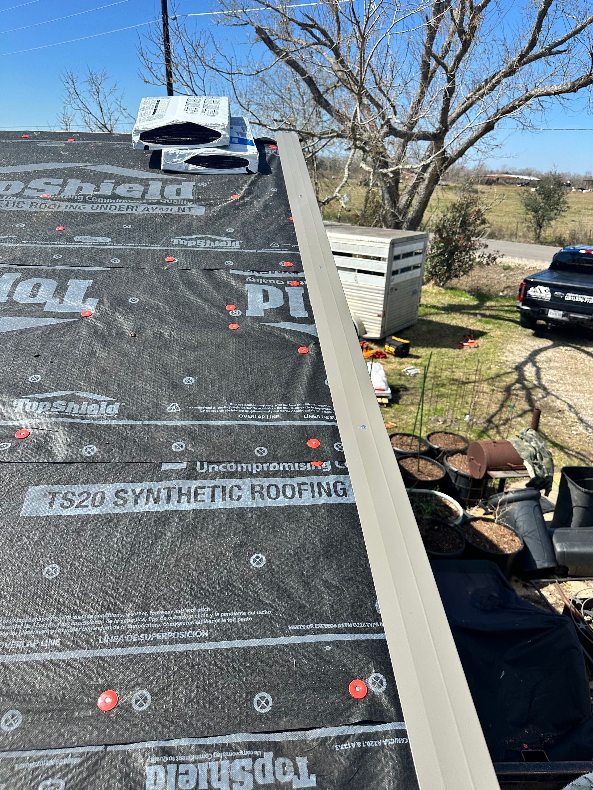 Rooftop with black synthetic roofing material, a metal trim piece, and a white vent against a blue sky.