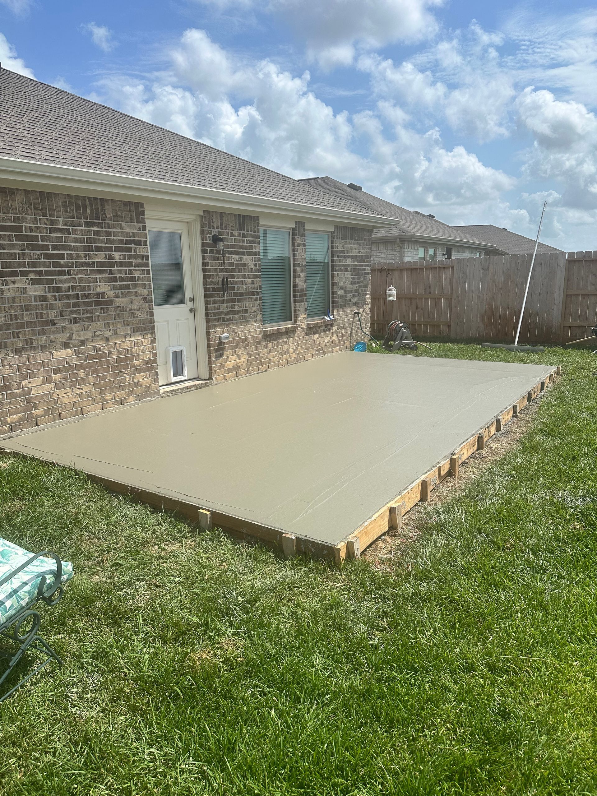 Freshly poured concrete patio next to a brick house, surrounded by wooden framing and grass.