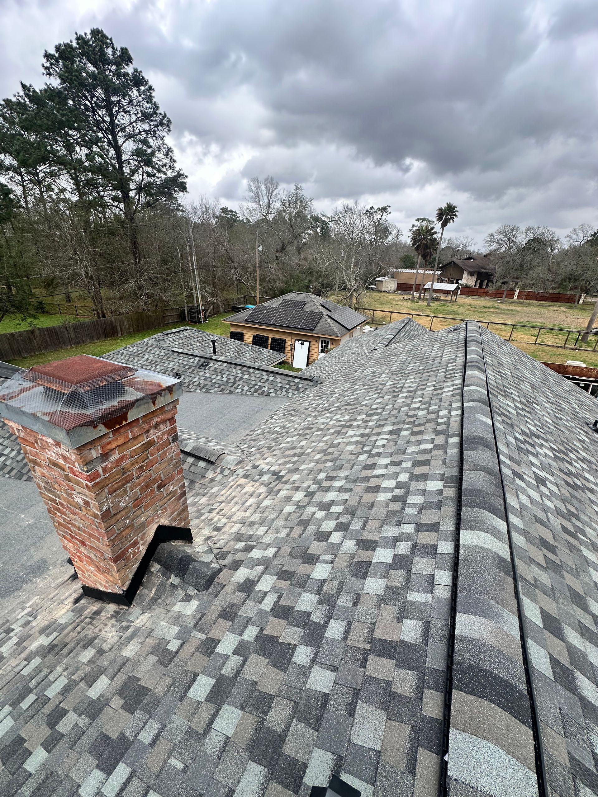 Newly installed asphalt shingle roof, chimney, and debris under overcast skies.