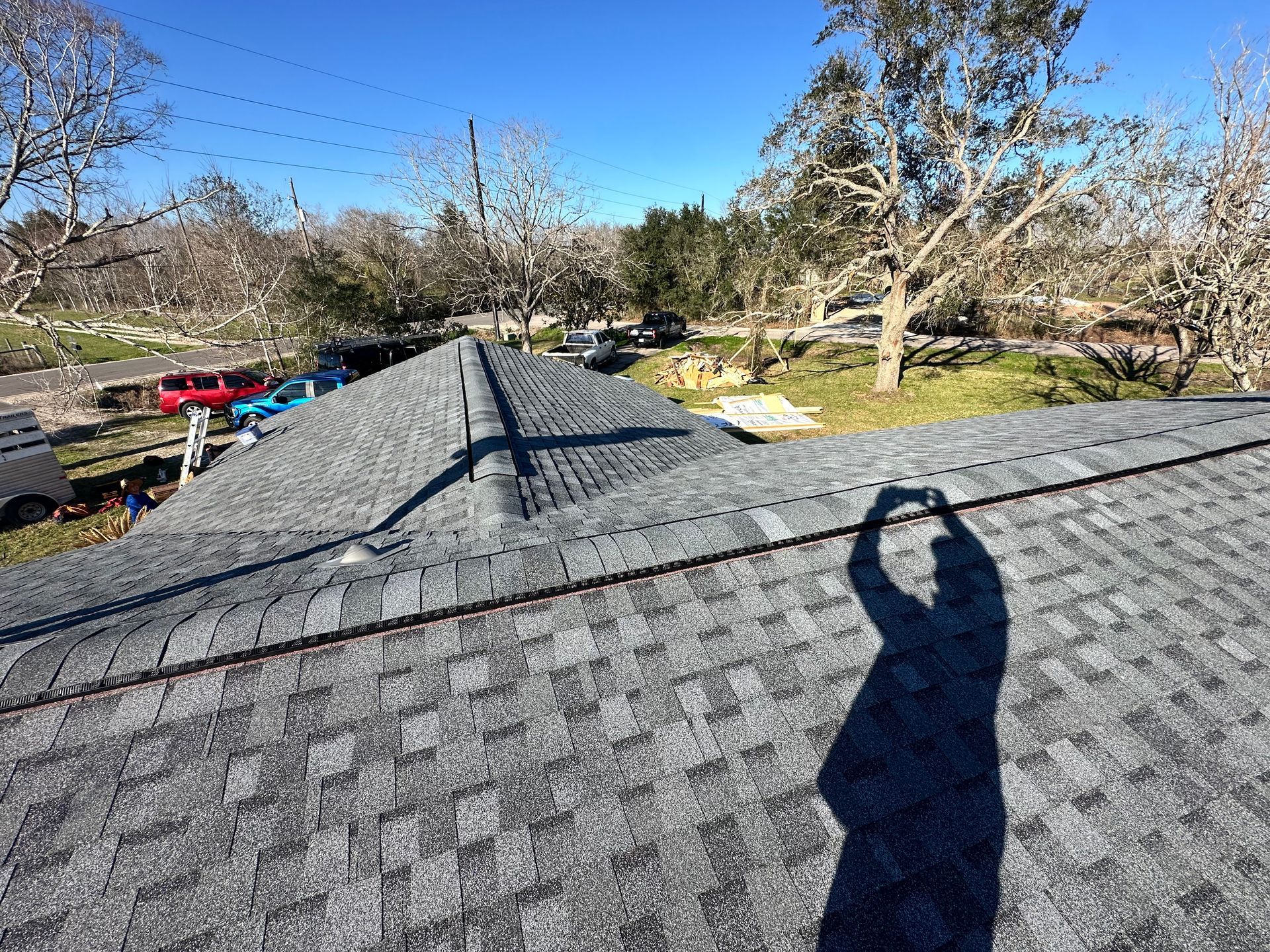 View of a gray shingle roof with a shadow of a person taking a photo on a sunny day.