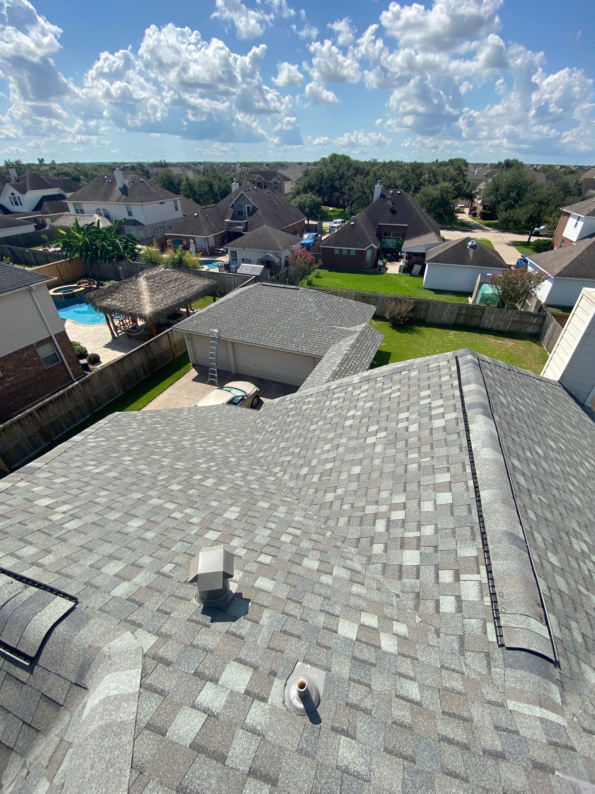 View of a suburban neighborhood, rooftops in focus with cloudy blue sky above.