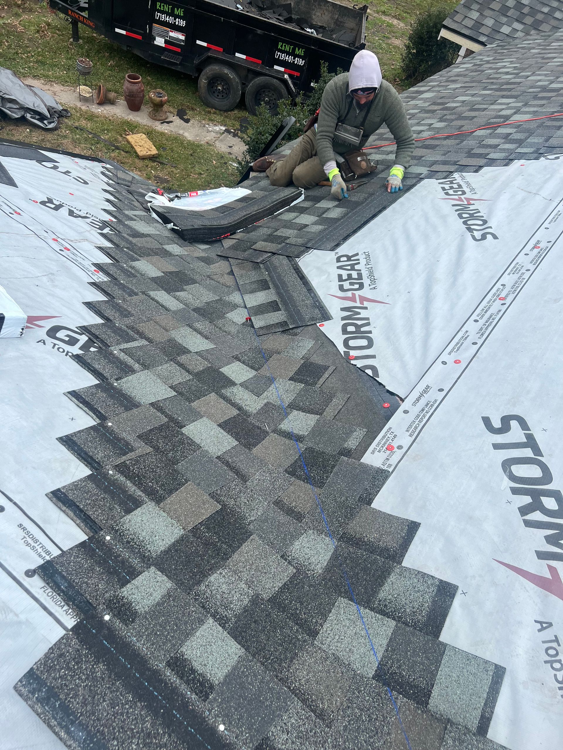 Person installing roofing shingles on a house roof. White underlayment and gray shingles.