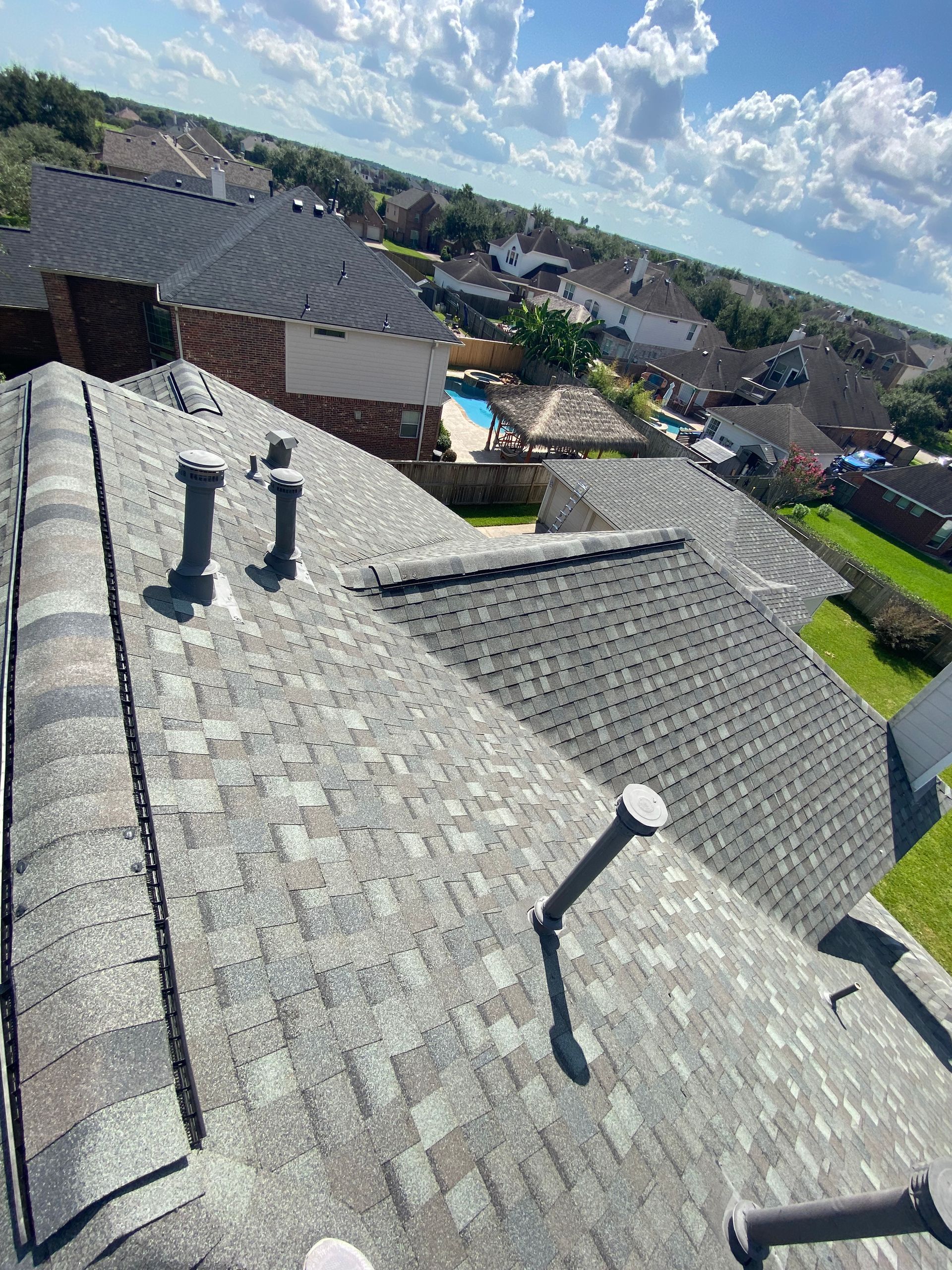 View of a residential rooftop with various vents against a backdrop of houses and blue sky.