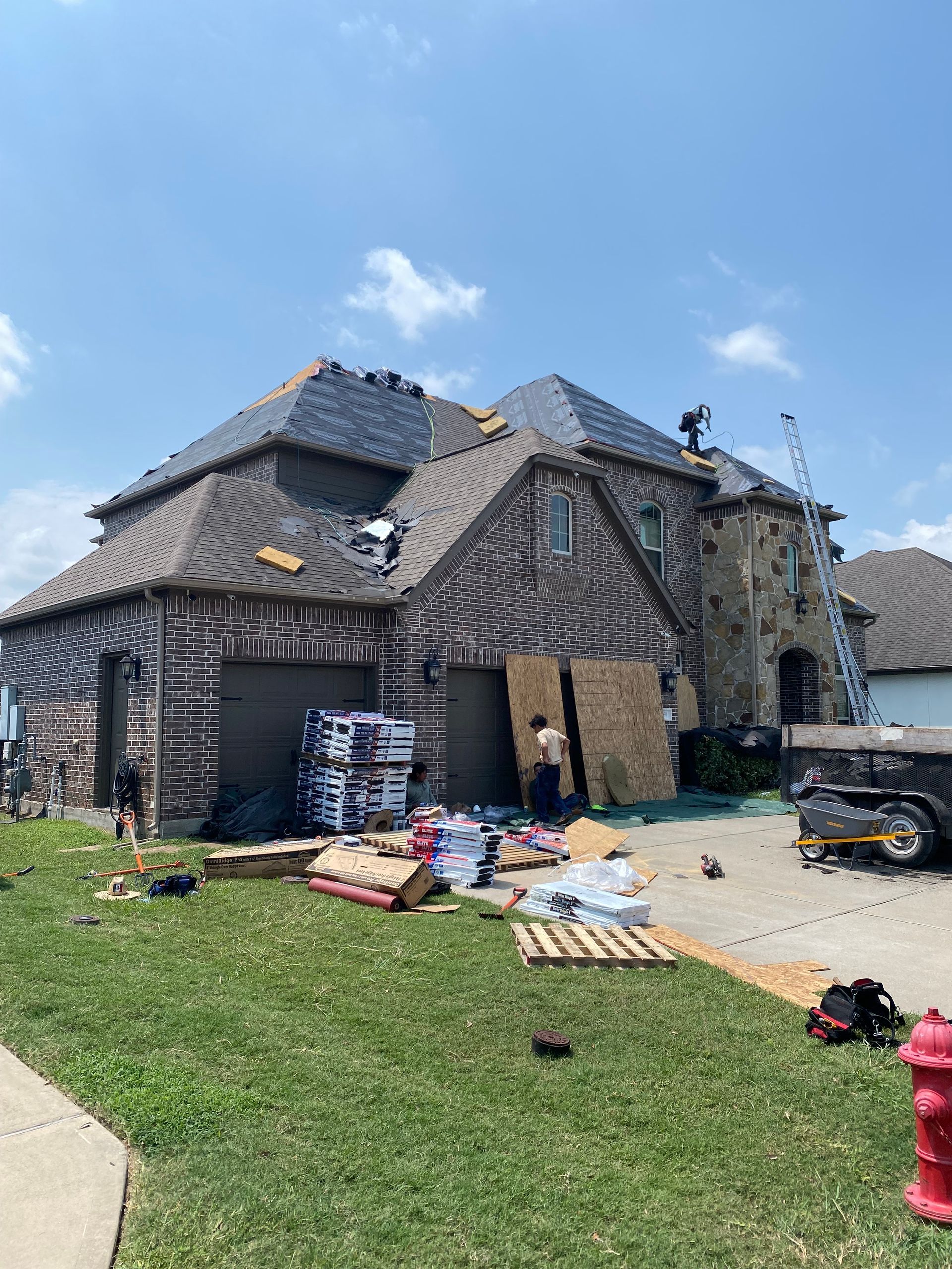 House roof replacement in progress with materials in the driveway on a sunny day.