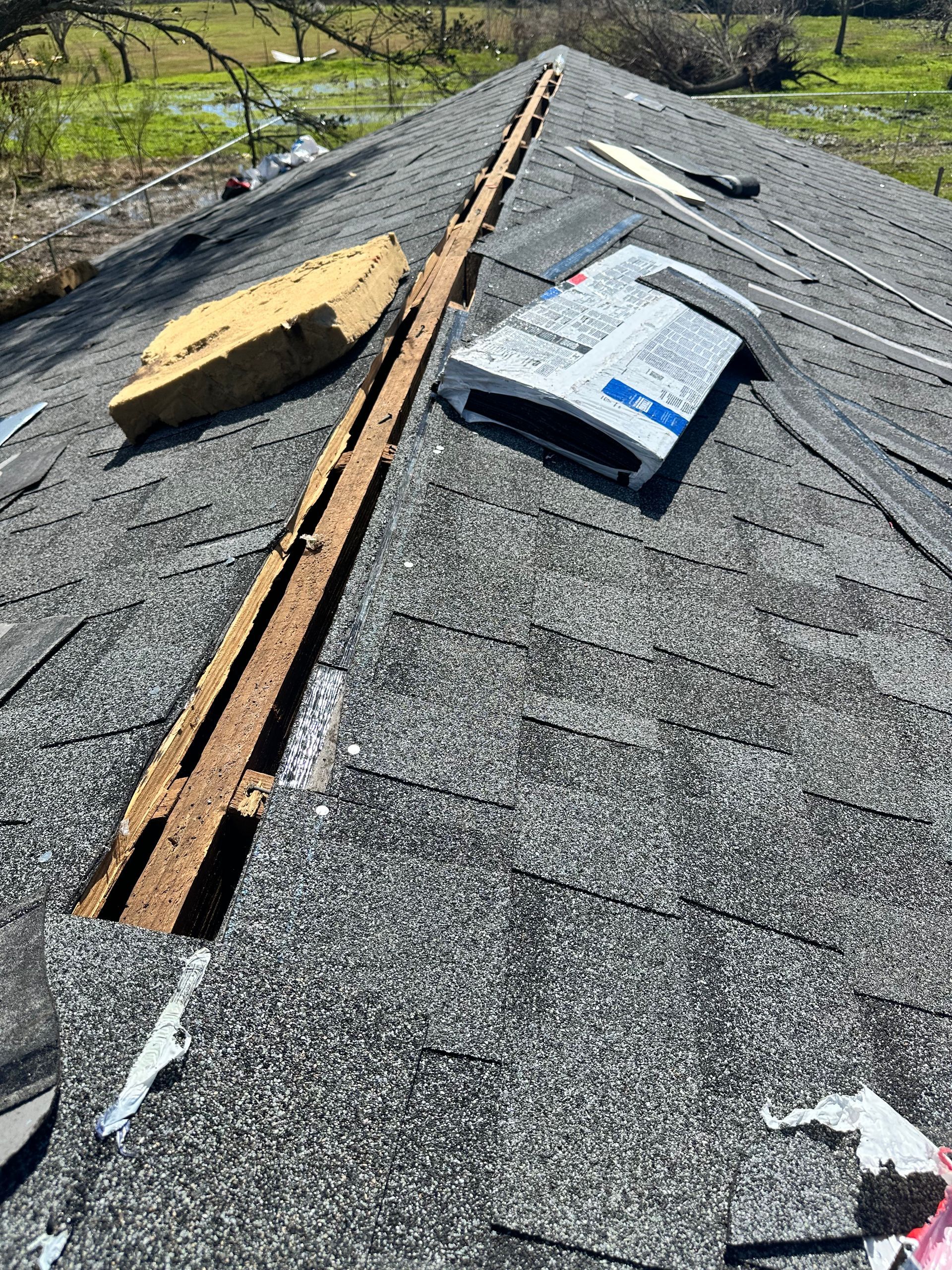 Close-up of roof damage. Missing shingles, exposed wood, and debris. Bright, sunny setting.