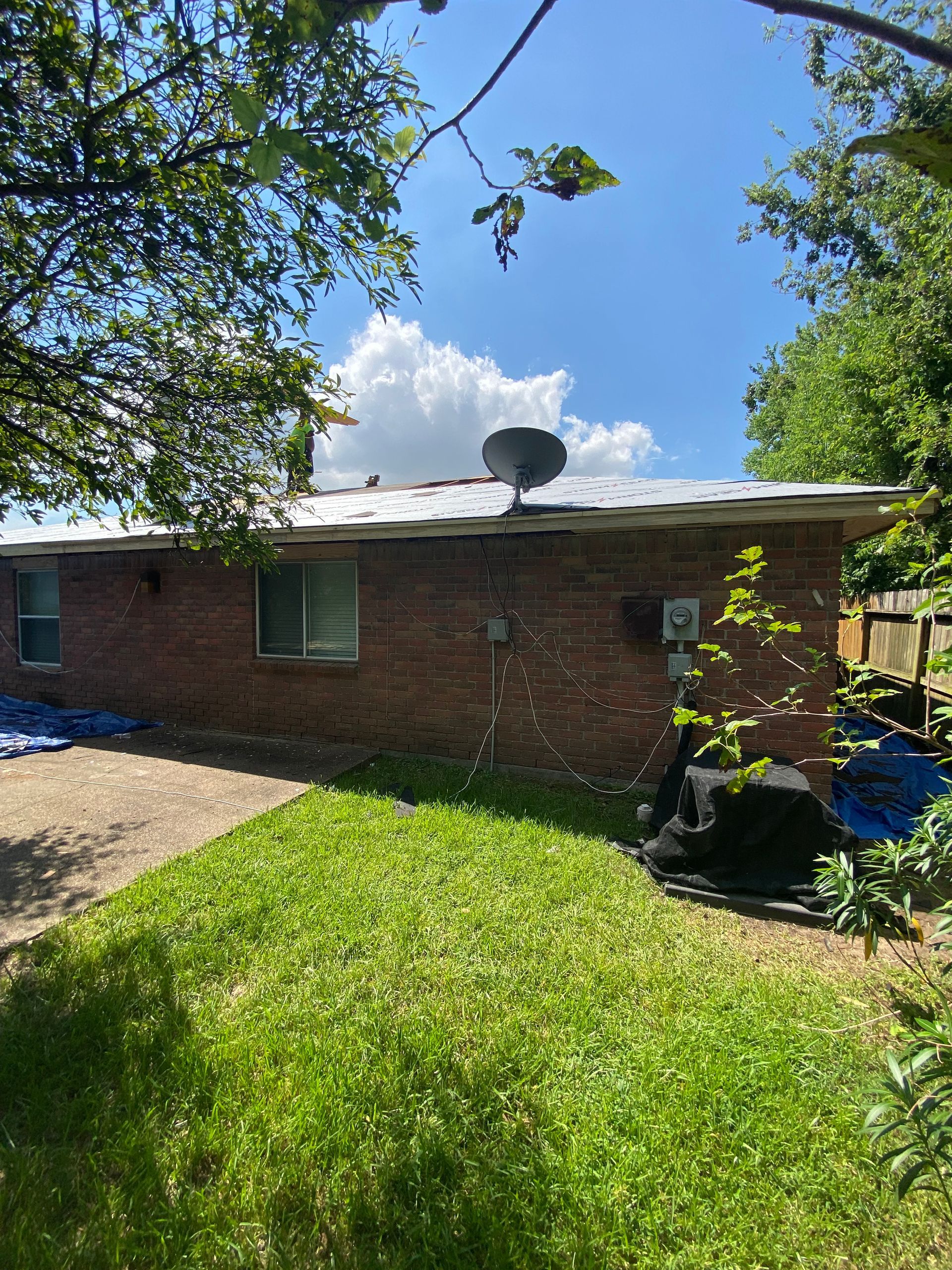 Red brick house with a satellite dish on the roof, viewed from a grassy yard on a sunny day.
