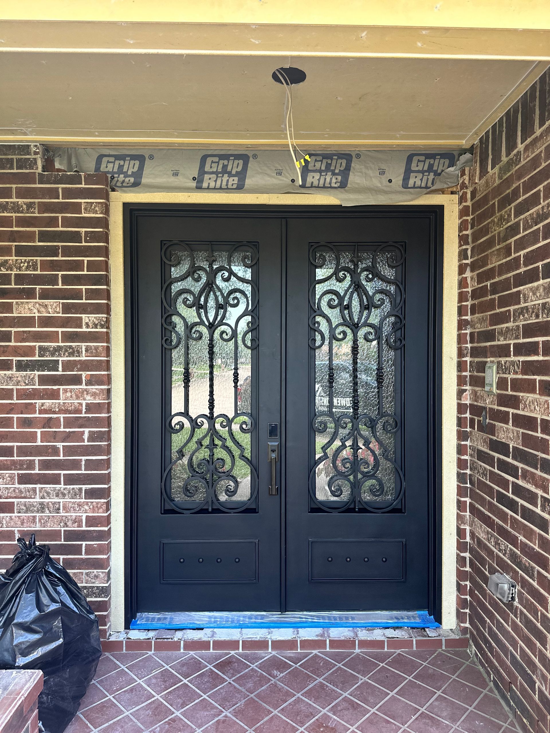 Black double entry doors with decorative ironwork, set in a brick facade under a covered porch.