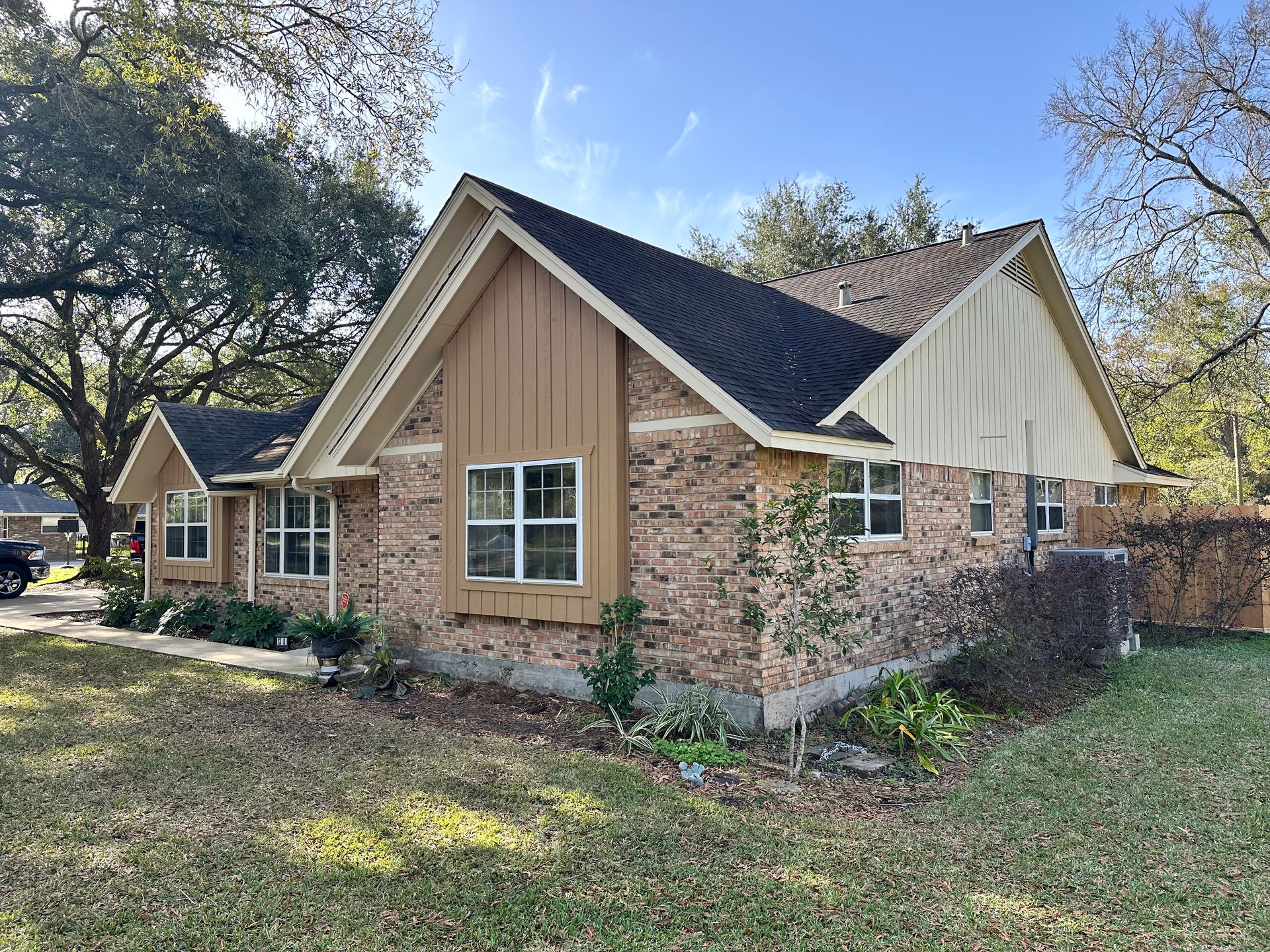 Brick house with brown and beige accents, set on a grassy lawn with trees in the background.
