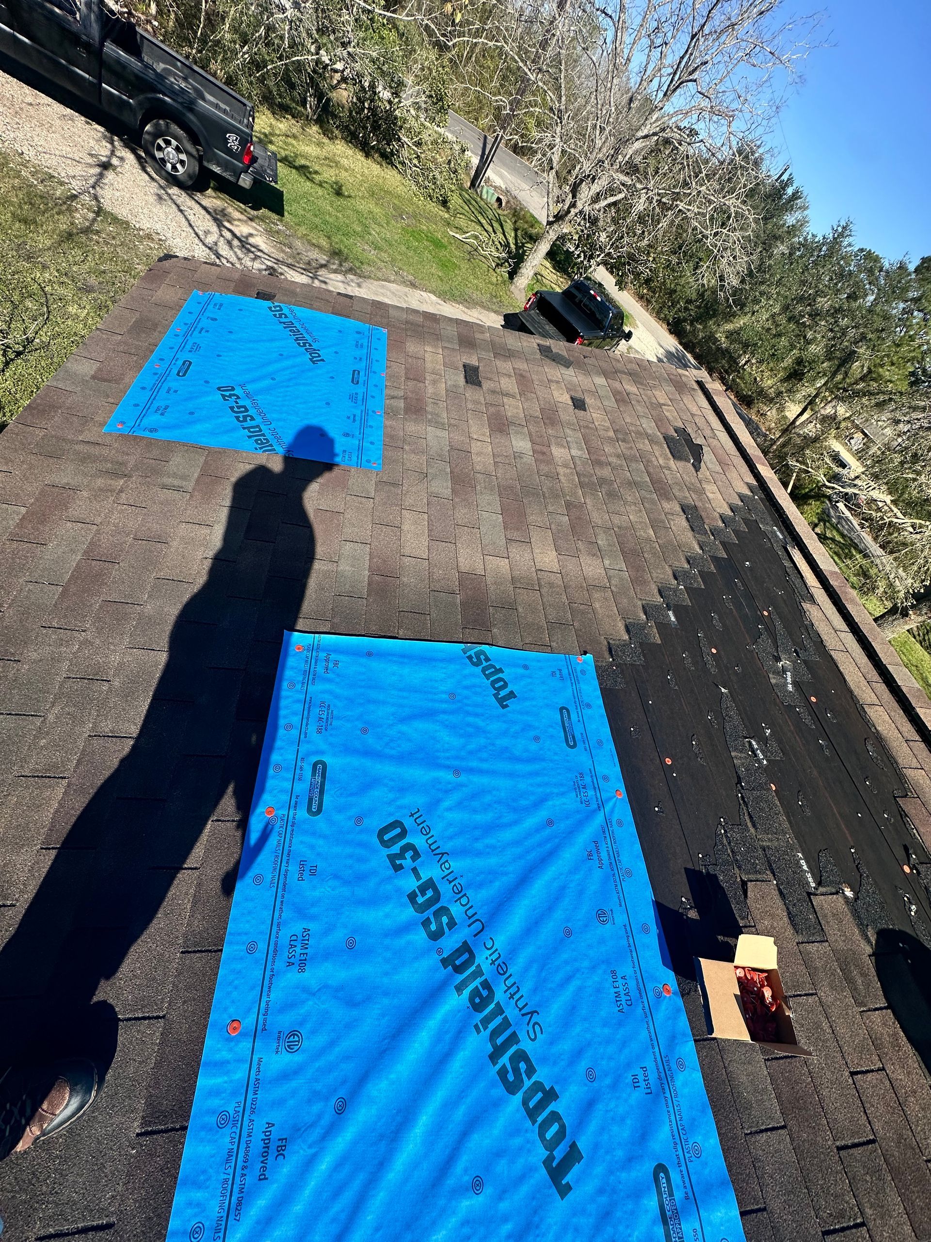 Roof with two blue tarps, likely for repair. A black vehicle sits nearby on a sunny day.