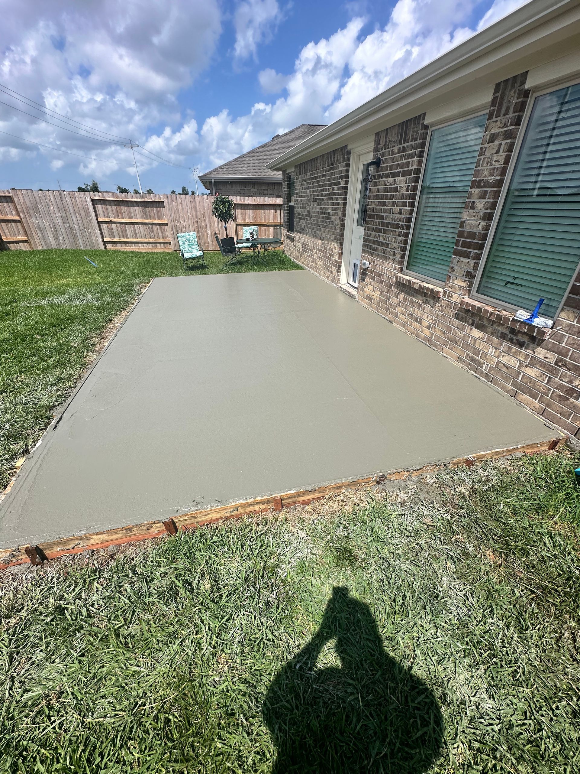 Newly poured concrete patio next to a brick house on a sunny day.