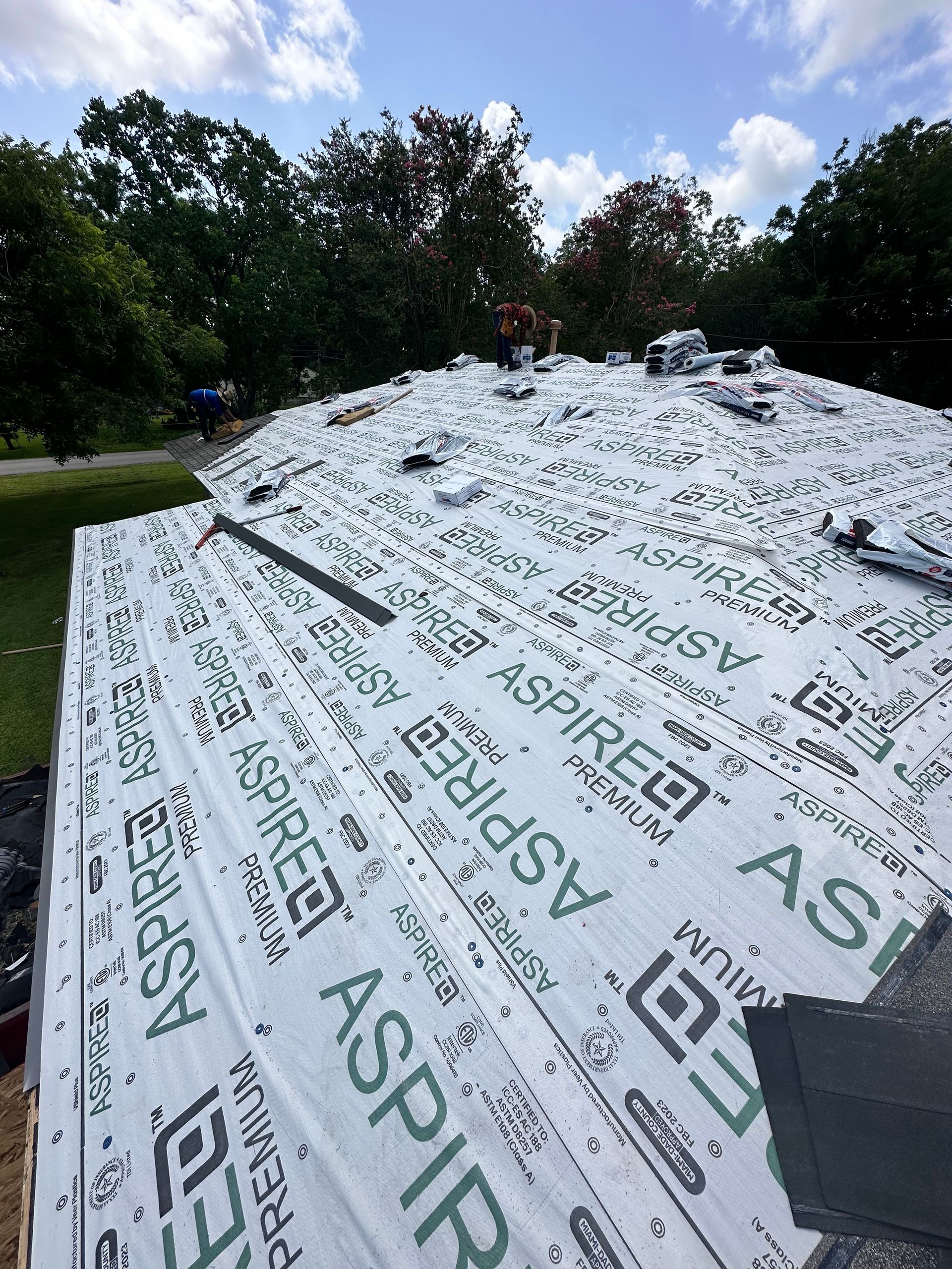 Roof with Aspire underlayment being installed. Workers visible, blue sky background.
