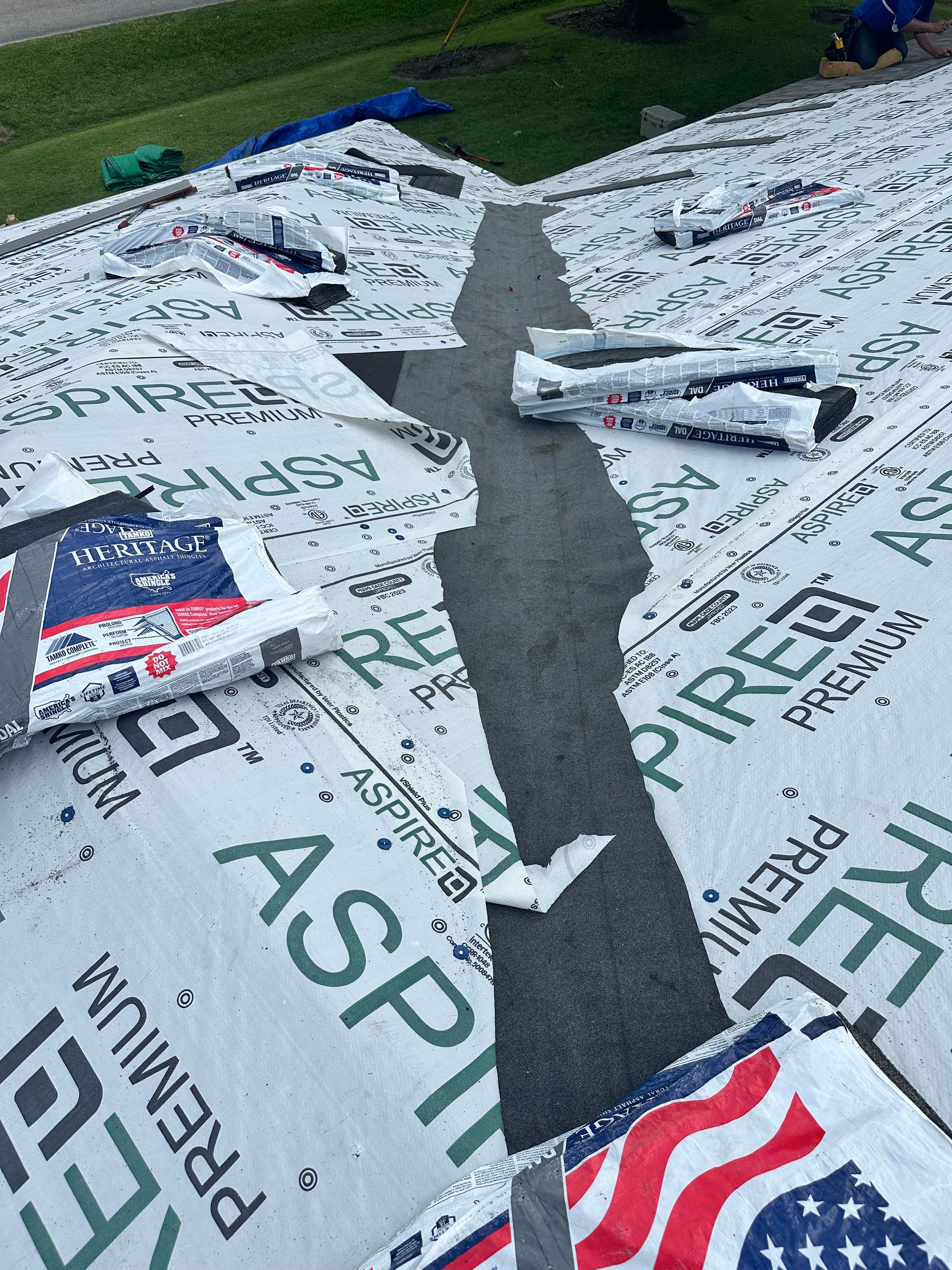 Roof partially covered with Aspire brand underlayment; American flag visible.