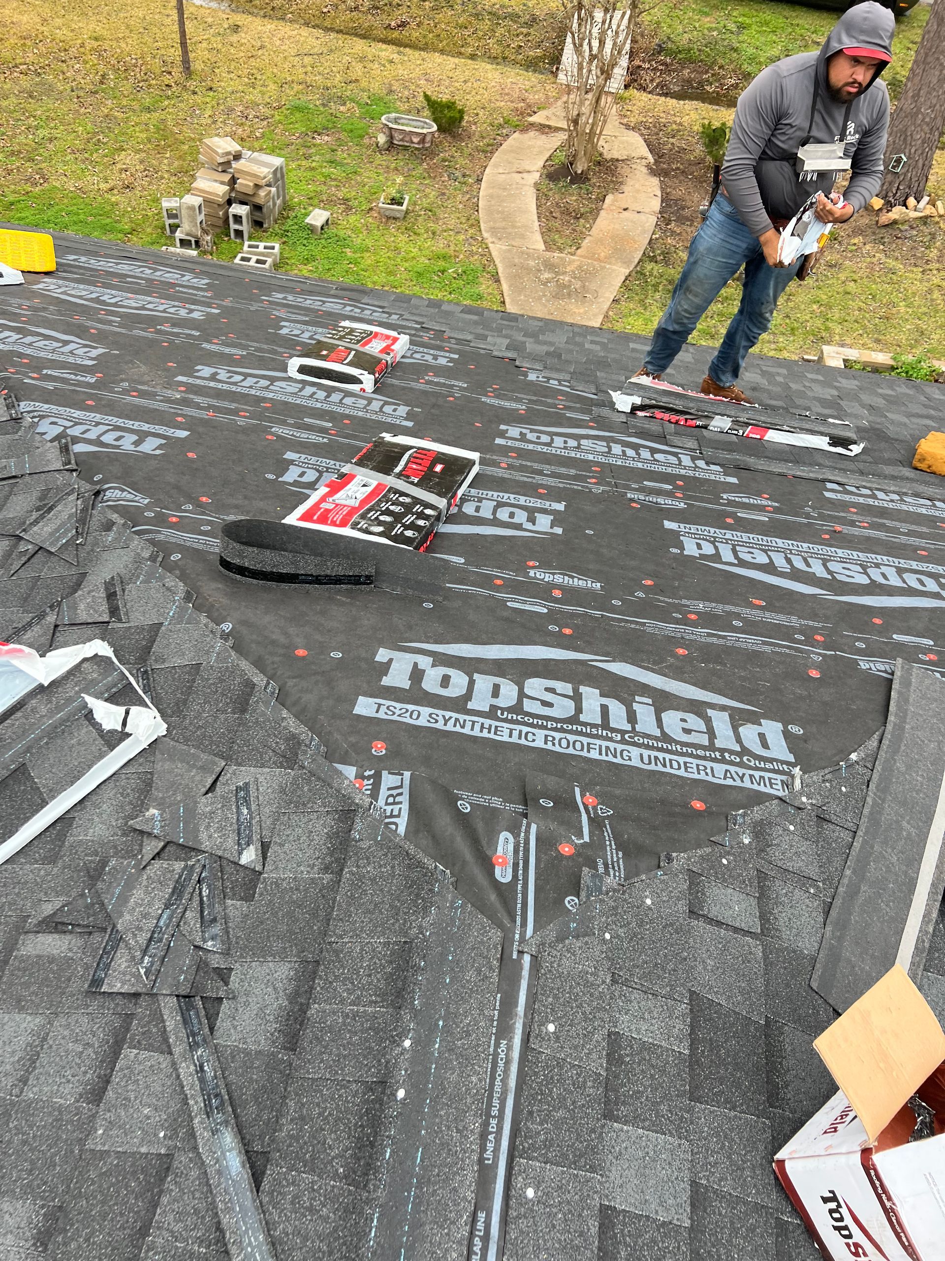 Roofer on a roof, installing asphalt shingles and protective underlayment.