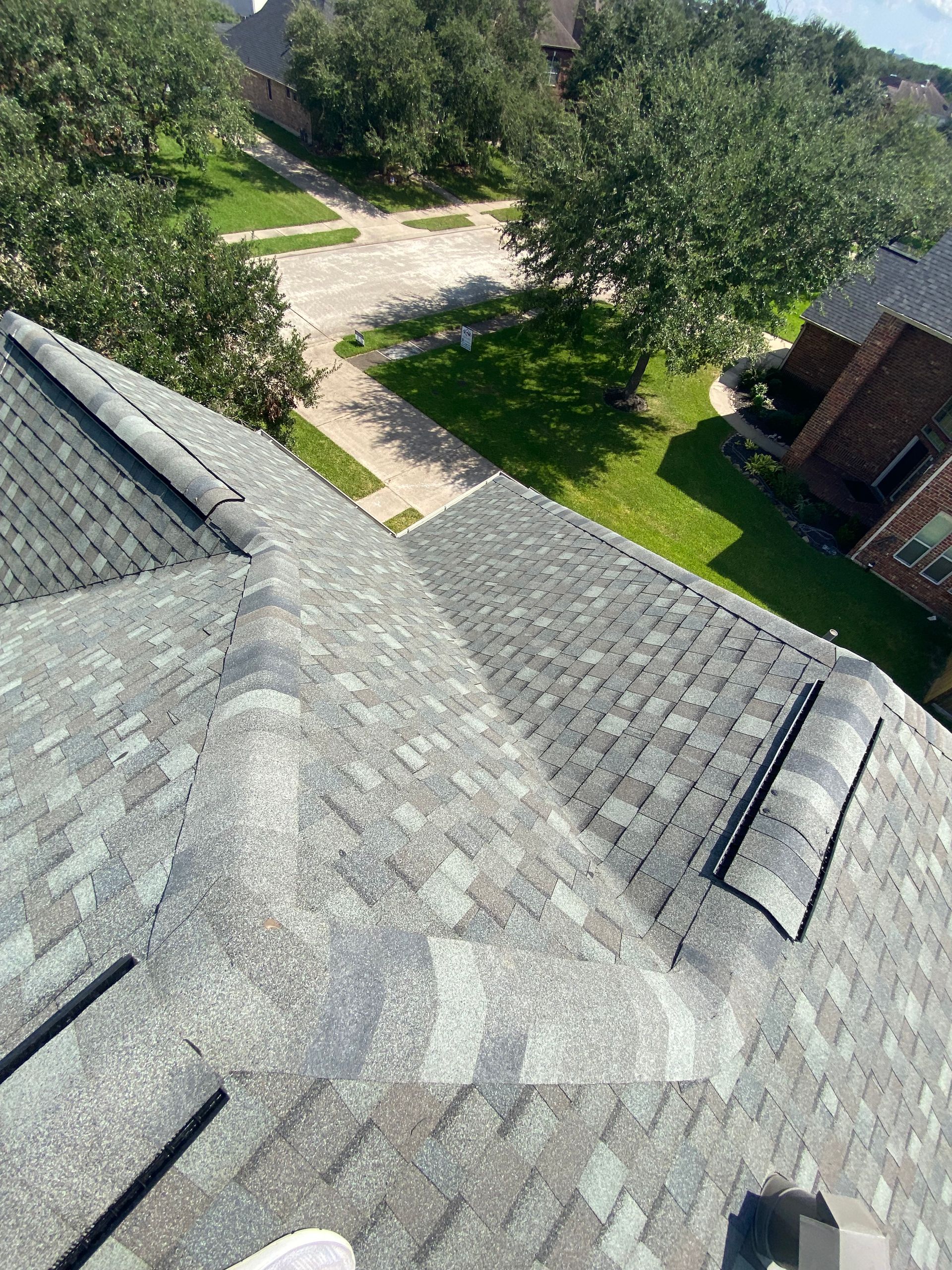 Overhead view of a roof with gray and green shingles, trees, and a pathway in the background.
