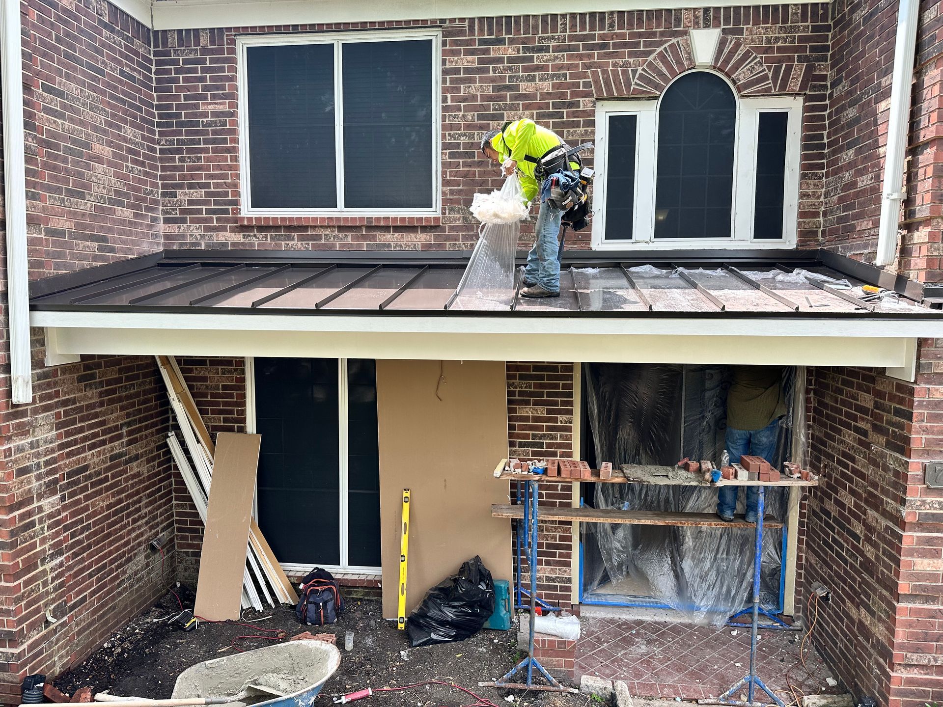 Construction worker on a roof, brick building. Windows covered, materials below.