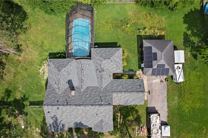 Aerial view of a house with gray roofs, a covered pool, driveway, and green lawn.