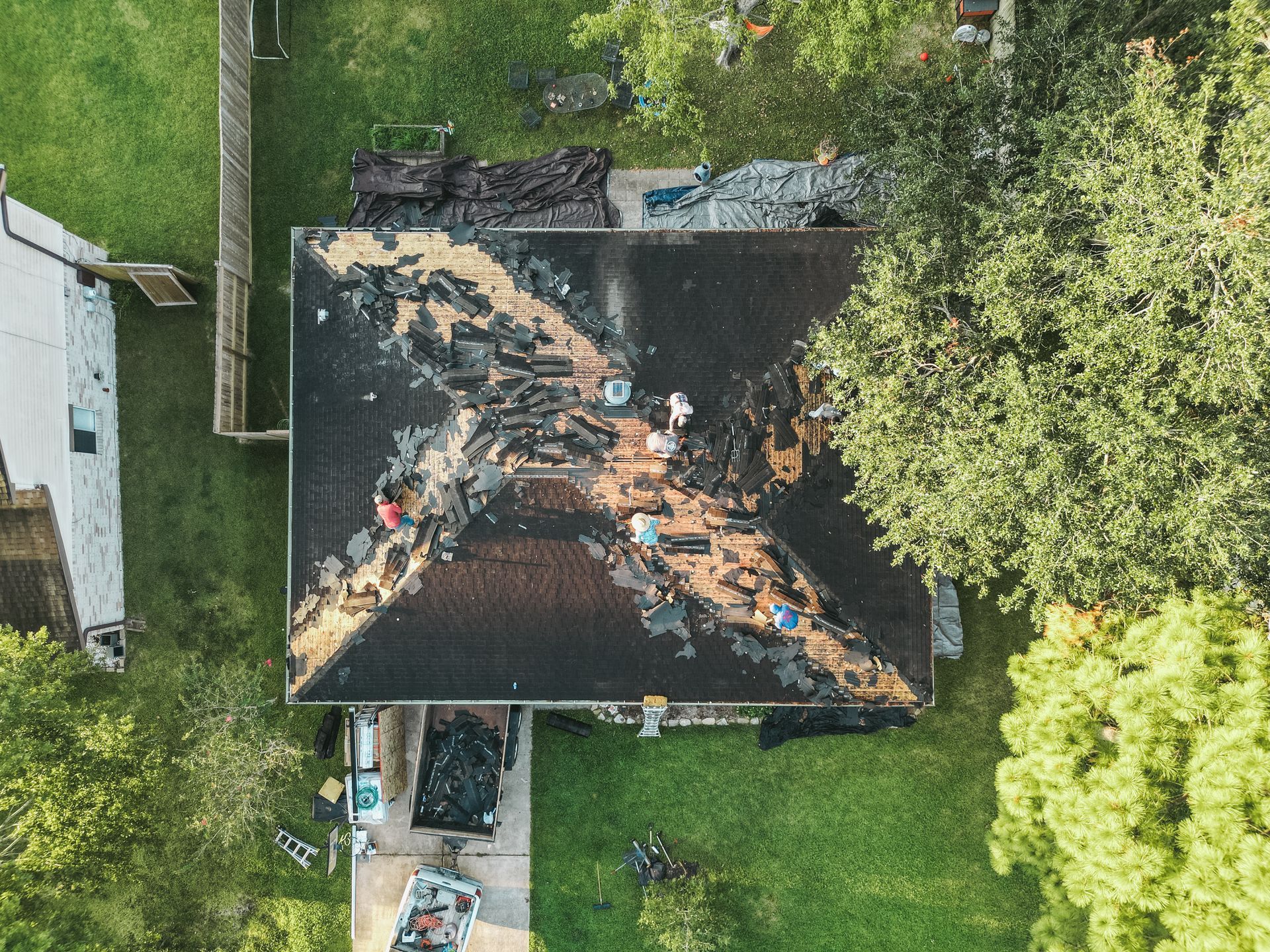 Overhead view of a house roof partially demolished, likely from fire damage. People work on the roof surrounded by debris.
