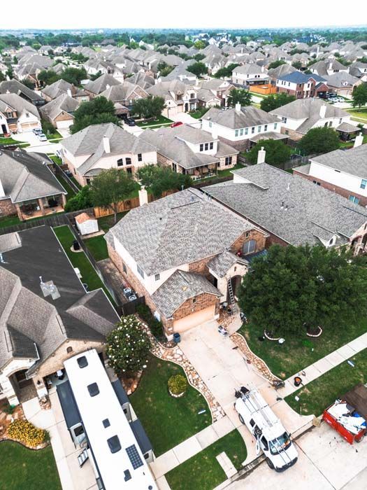 Aerial view of a suburban neighborhood with rows of houses, driveways, and streets under cloudy skies