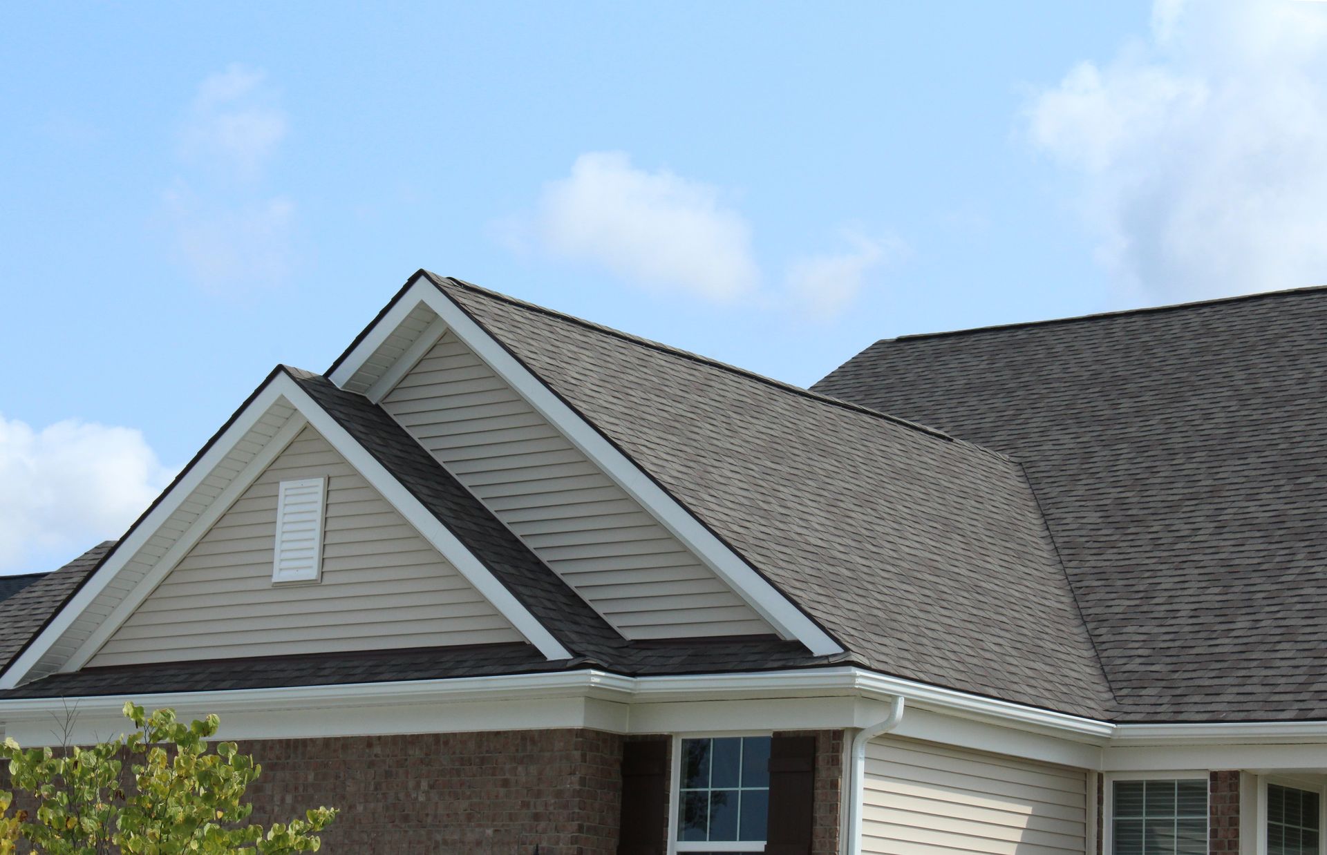 House roof with brown shingles, tan siding, and a blue sky.
