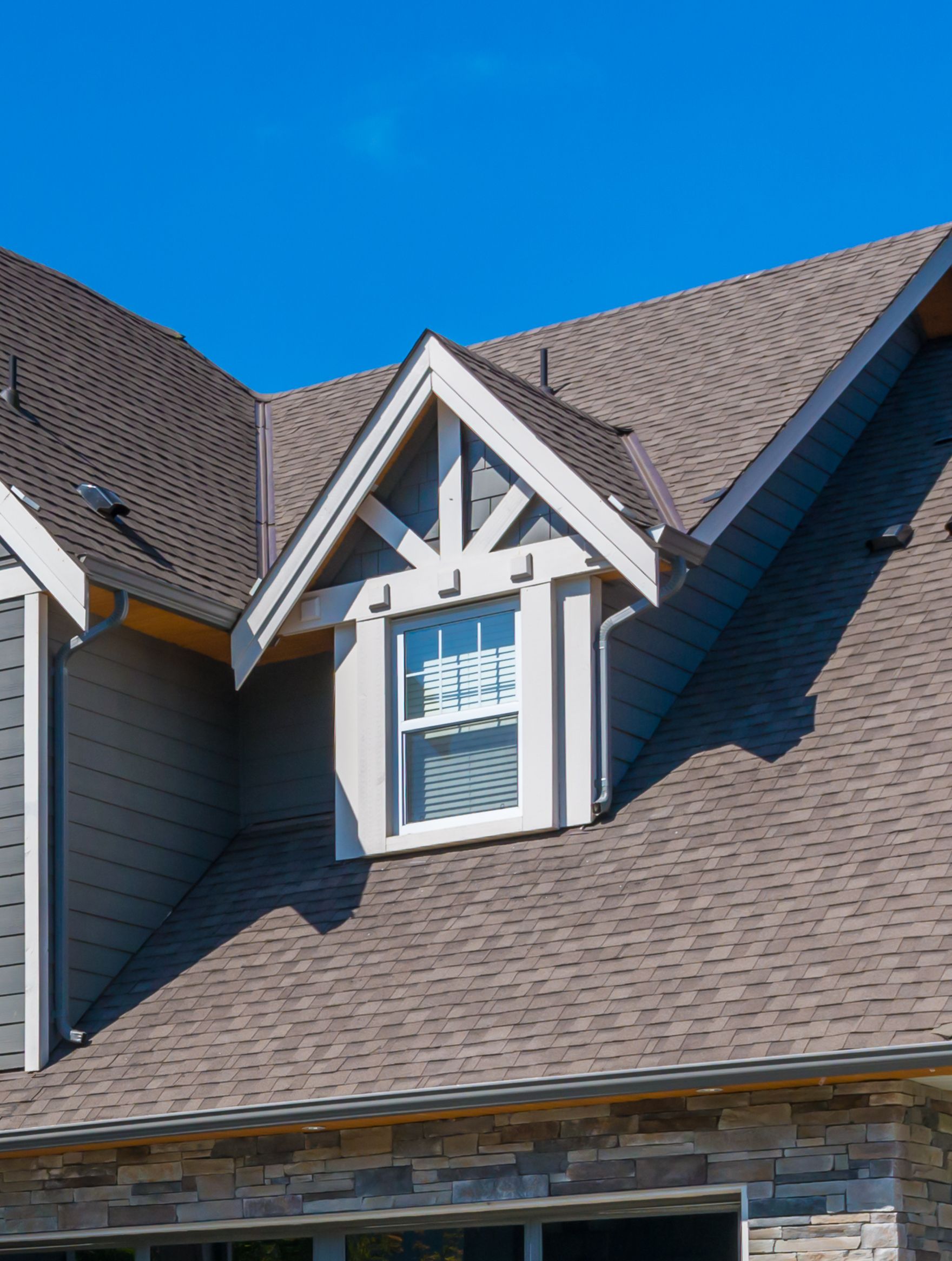 Gabled house with dormer window, gray roof, blue sky.