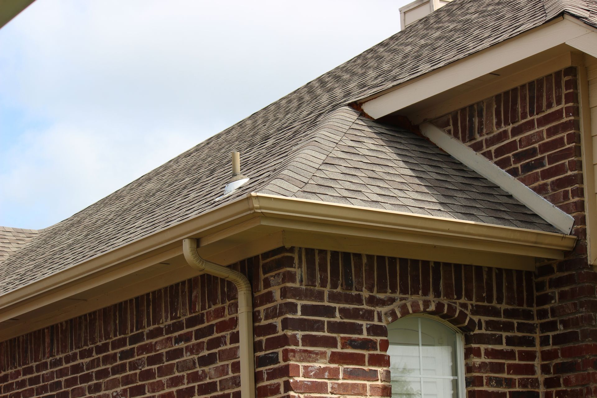 Brick house with brown roof and beige gutters.
