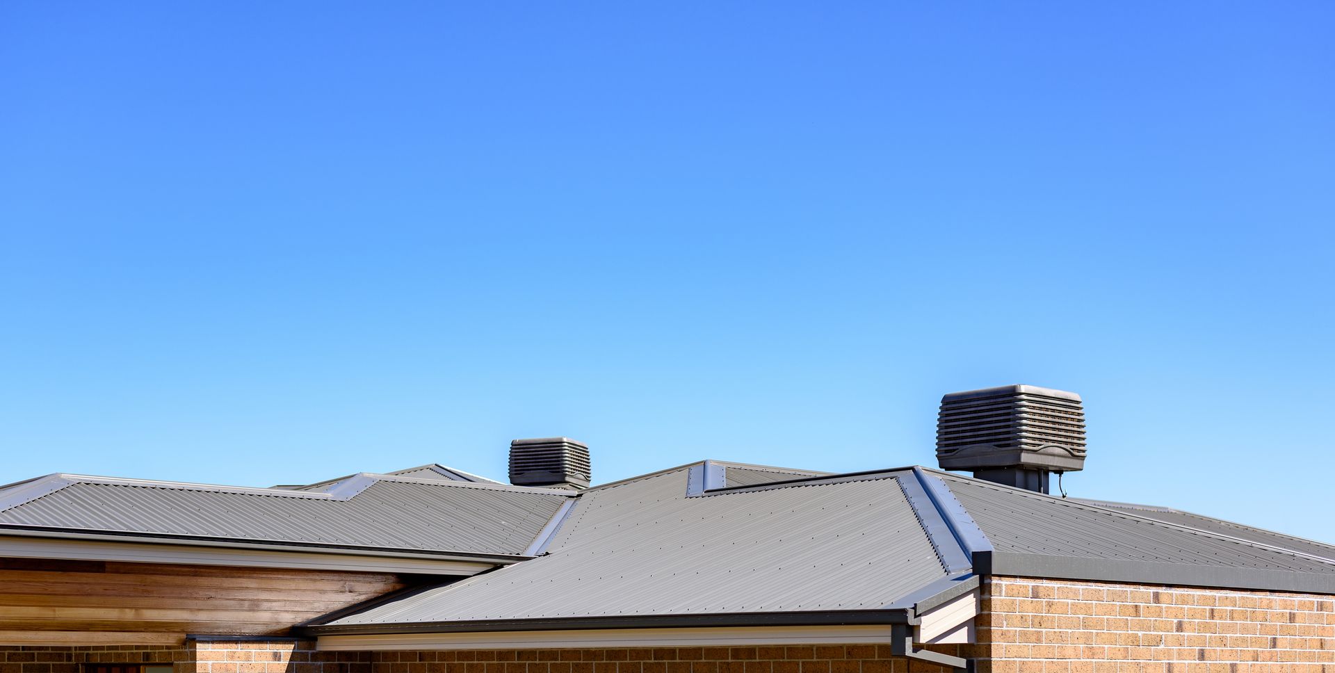 Gray metal roof with two square vents, against a clear blue sky. Brick building.