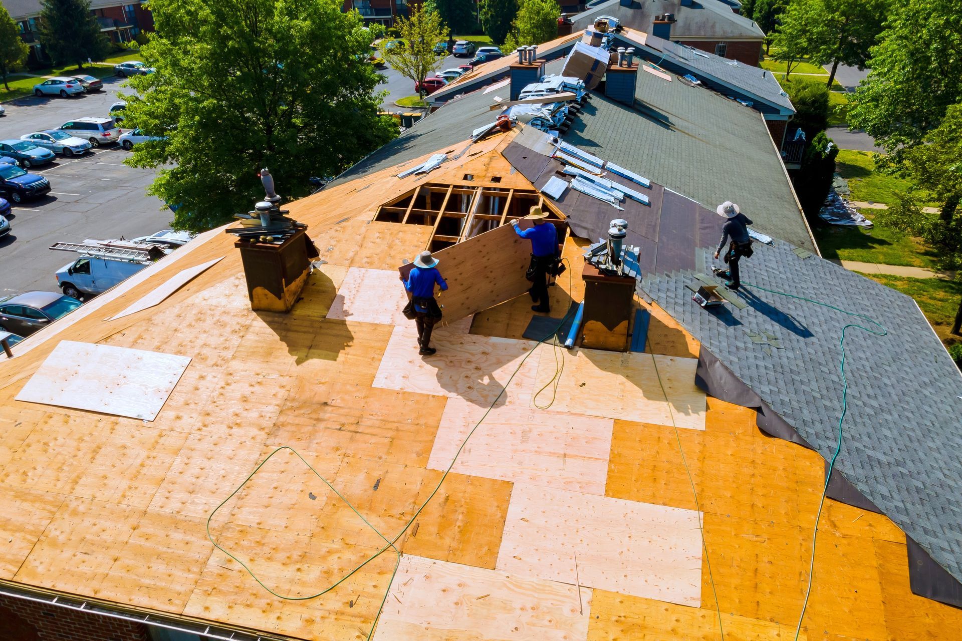 Roofers installing new shingles on a building with three chimneys; sunny outdoor setting.