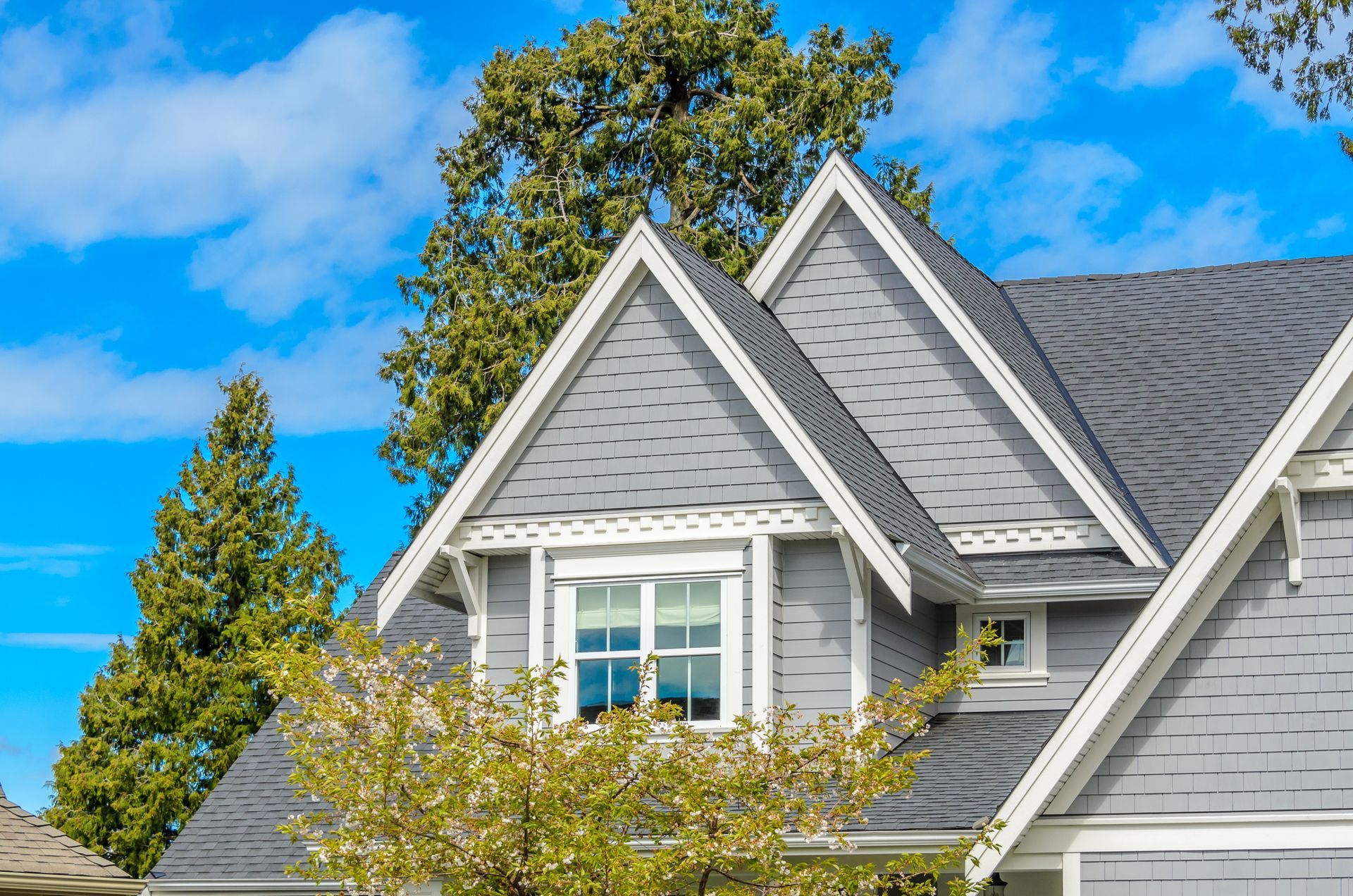 Gray house with white trim, dormer window, and blue sky.